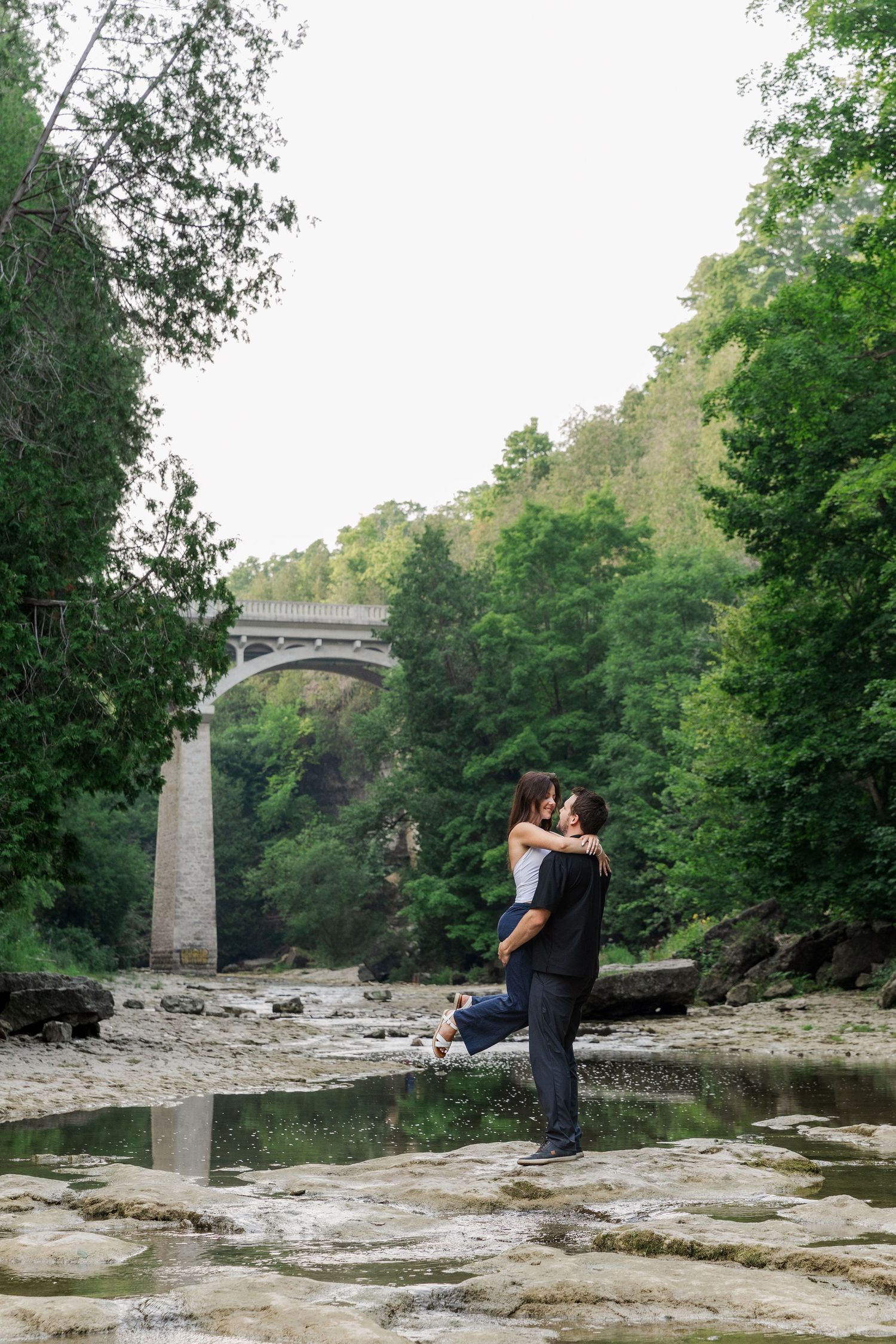 Candid engagement photo of a couple spinning around on the river bed of the elora gorge in elora, ontario.