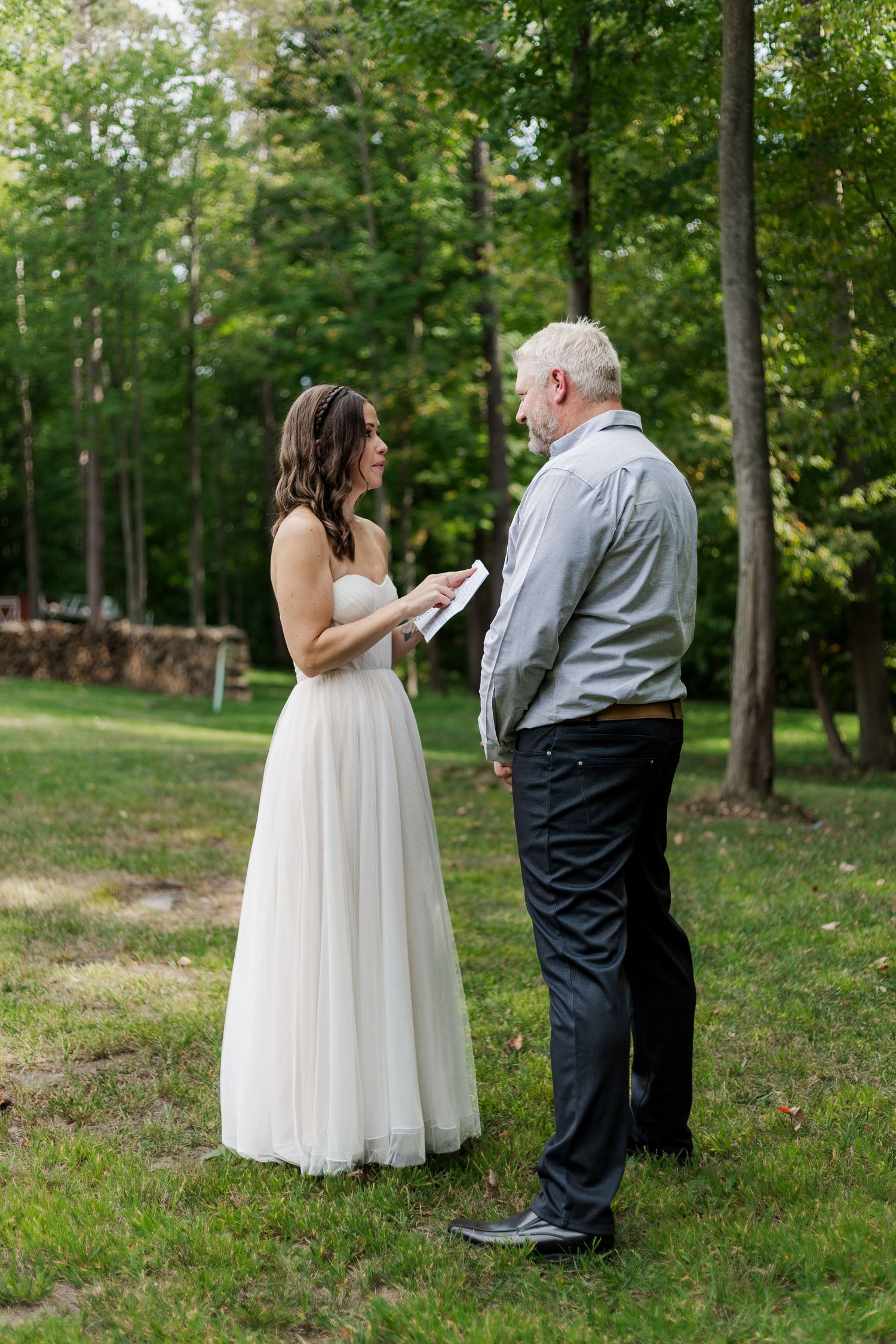 Candid wedding photo of bride and groom reading their private vows together surrounded by large green trees near woodstock, ontario.