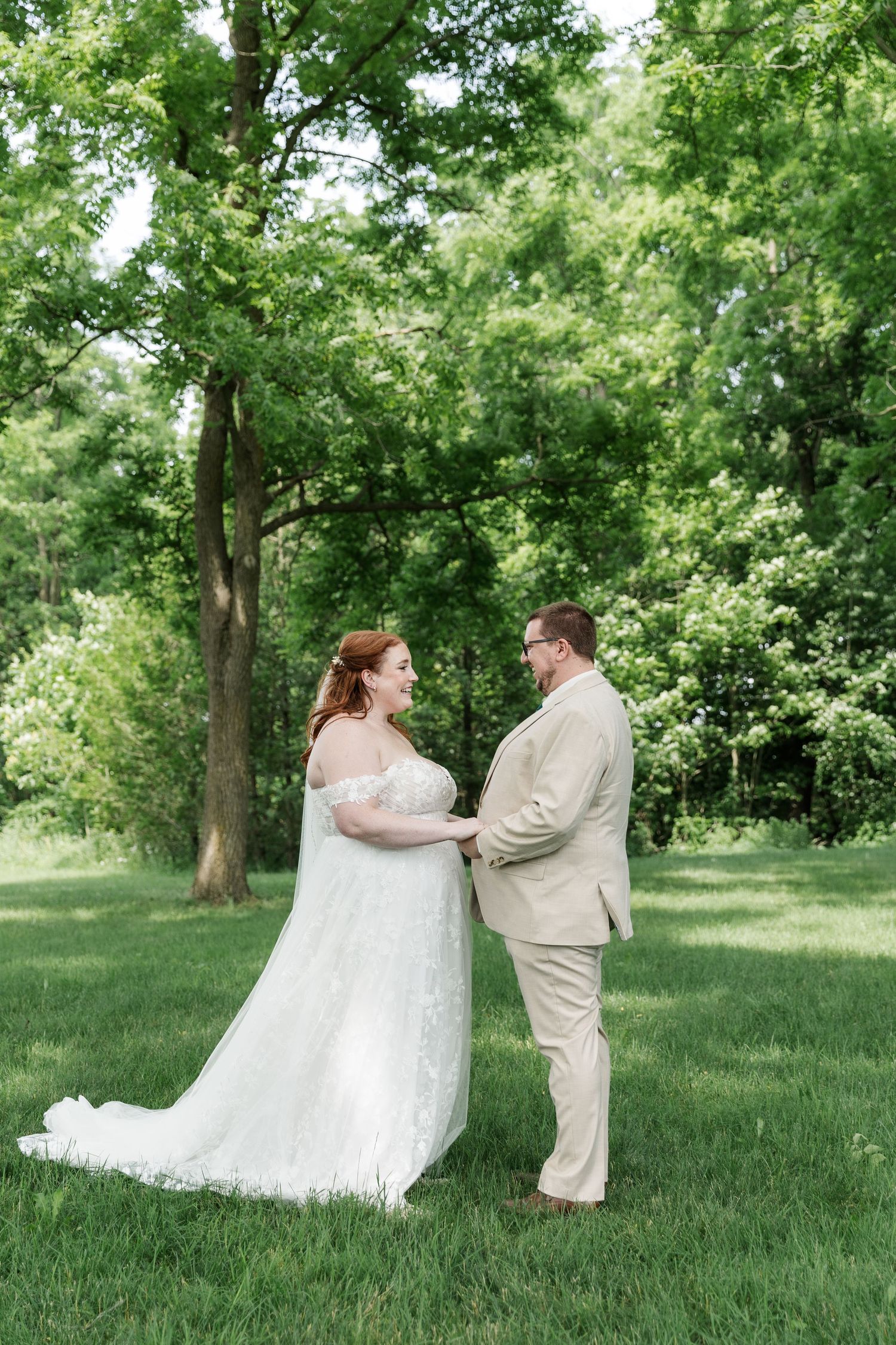 Bride and groom hold hands during a first look on their wedding day surrounded by greenery and large trees in Kitchener, Ontairo.