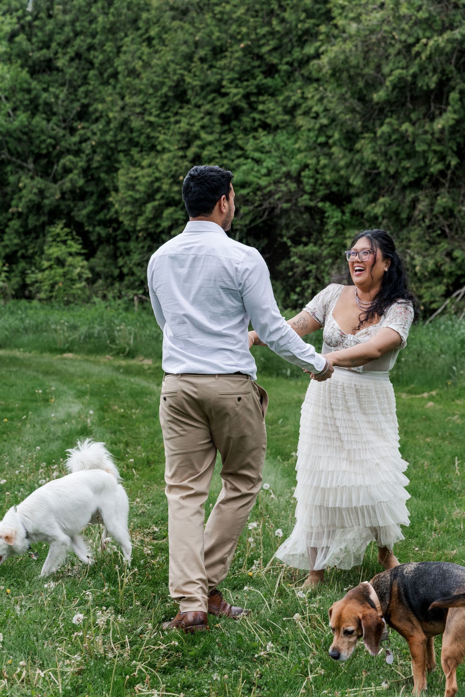A couple dances in a grassy field with their two dogs playing around them at The Guelph Arboretum.