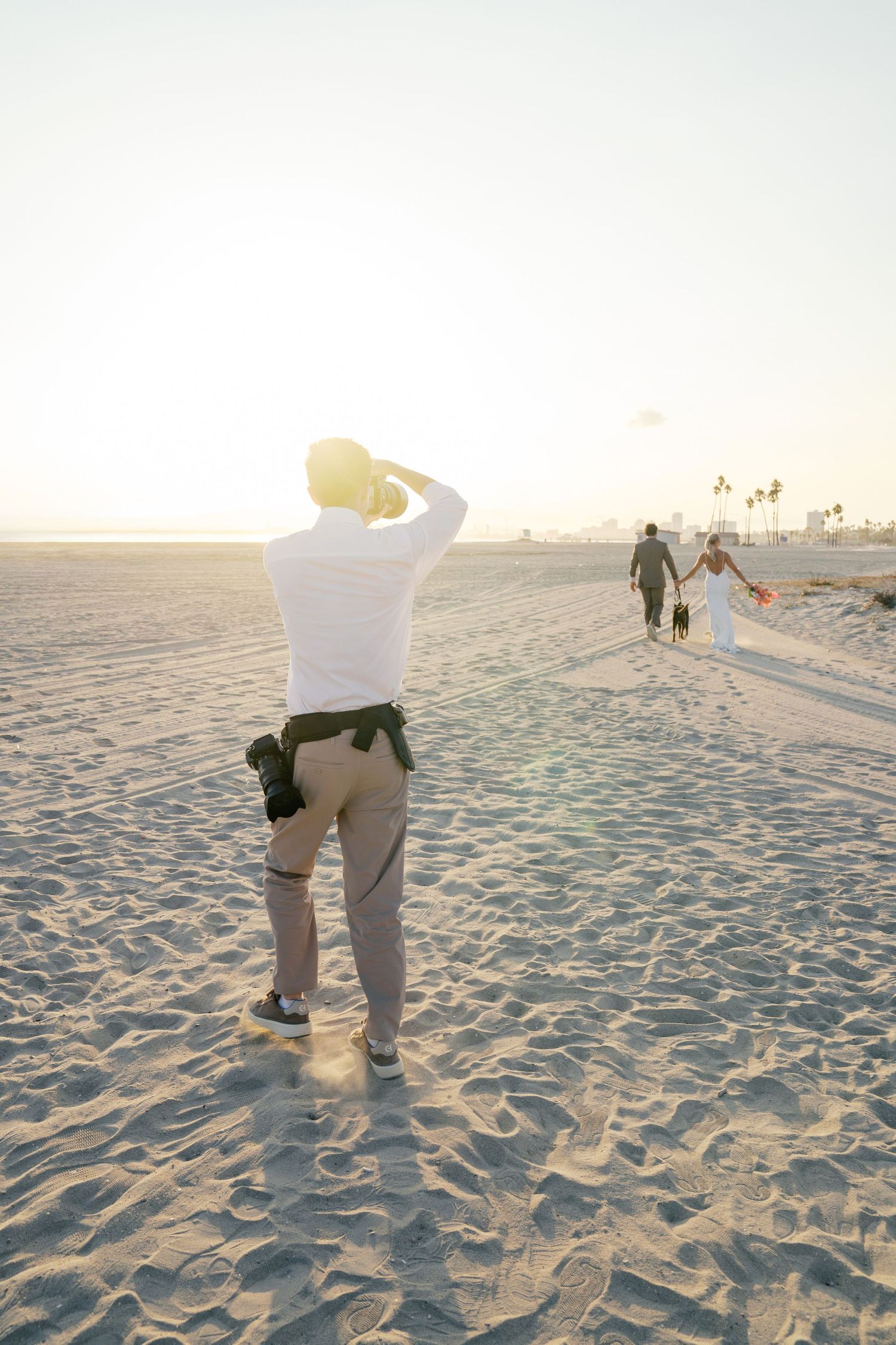 Photographer captures people on a sandy beach at sunset as warm light bathes the scene in golden hues.