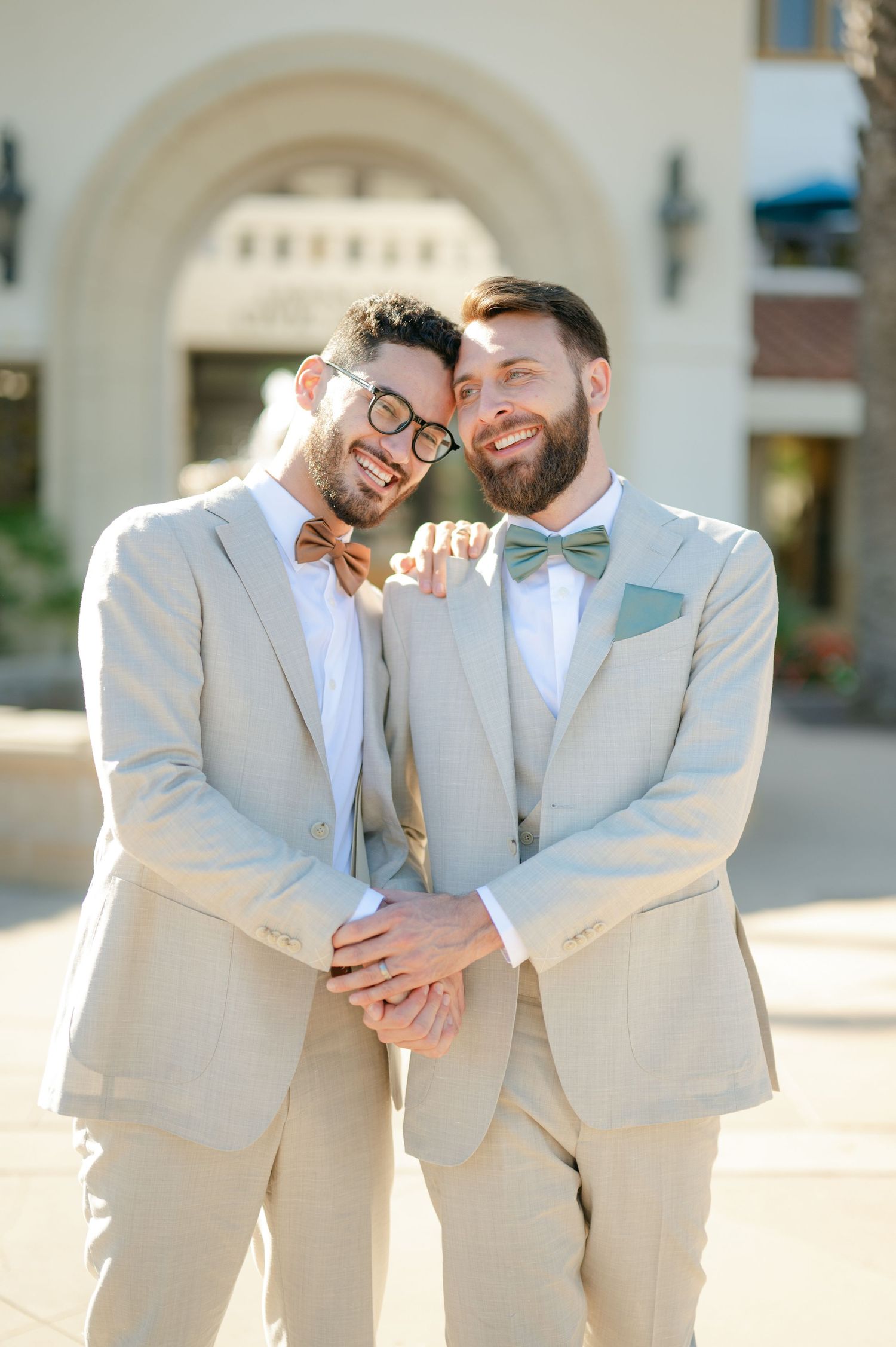 Two grooms in matching light beige suits share a joyful moment together.