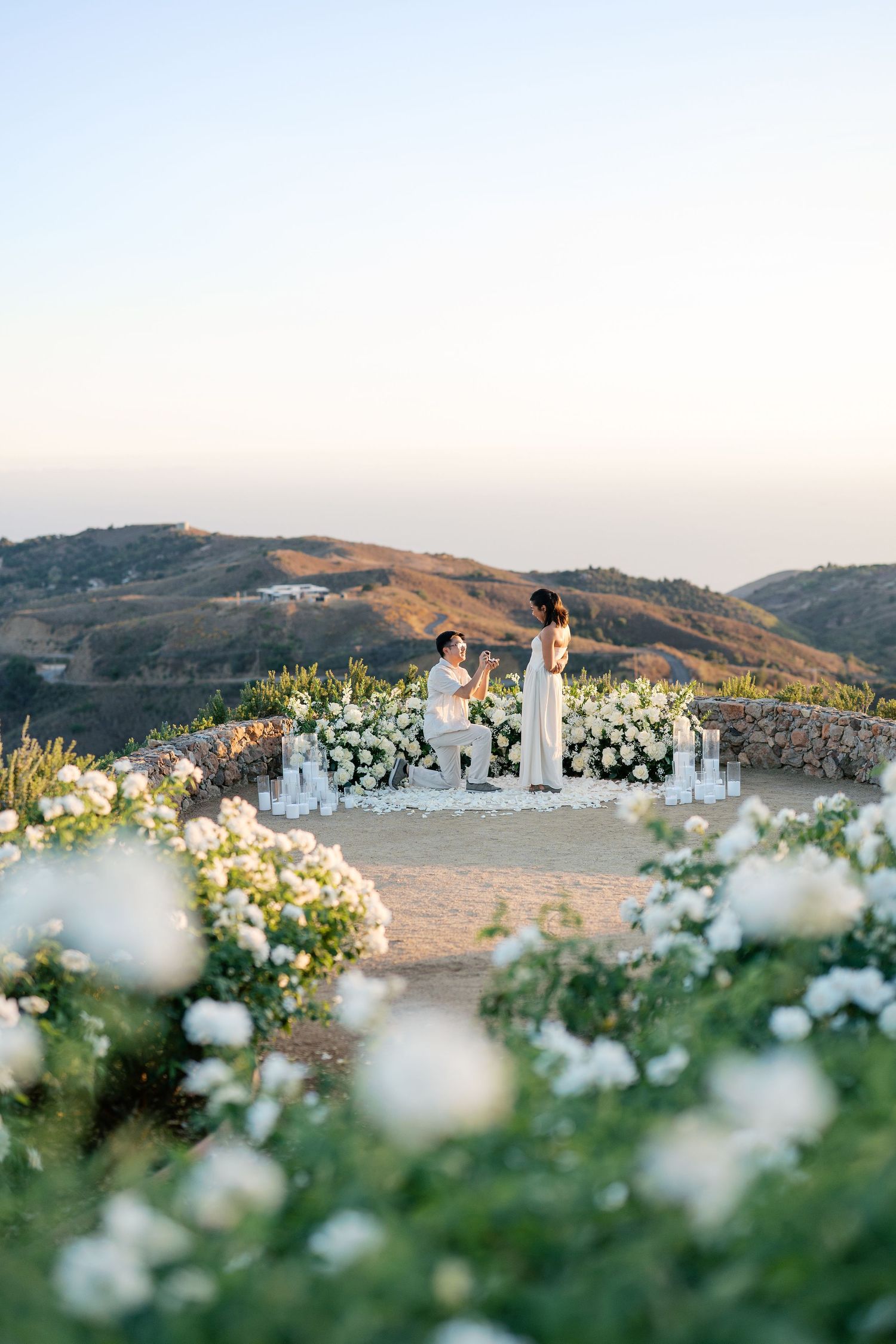 Outdoor wedding ceremony altar decorated with white flowers against scenic mountain backdrop at sunset.
