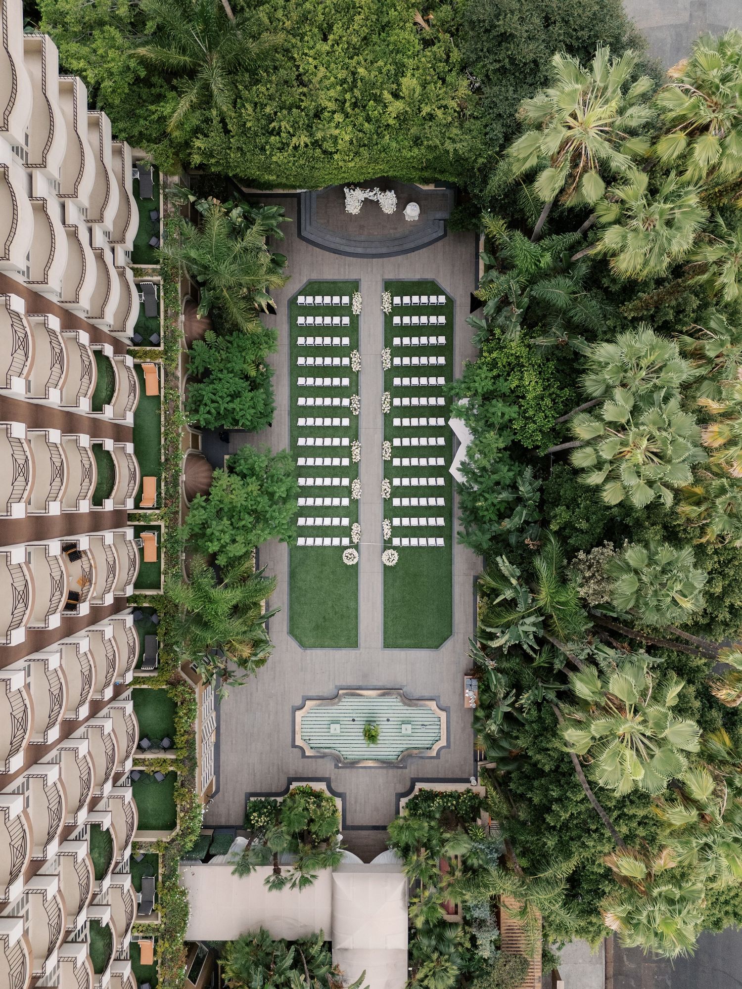 Aerial view of a symmetrical hotel courtyard with rows of lounge chairs, a fountain, and lush tropical greenery.