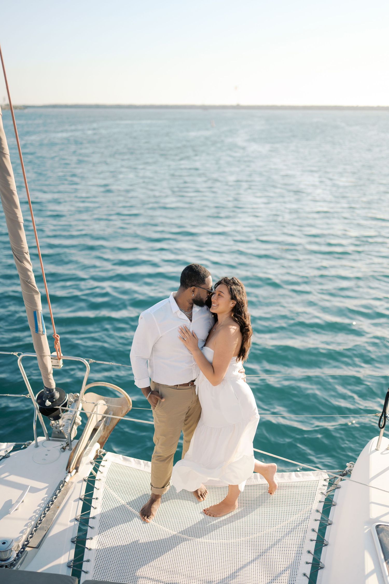 Romantic couple embracing on a white sailboat deck with turquoise ocean waters in the background.