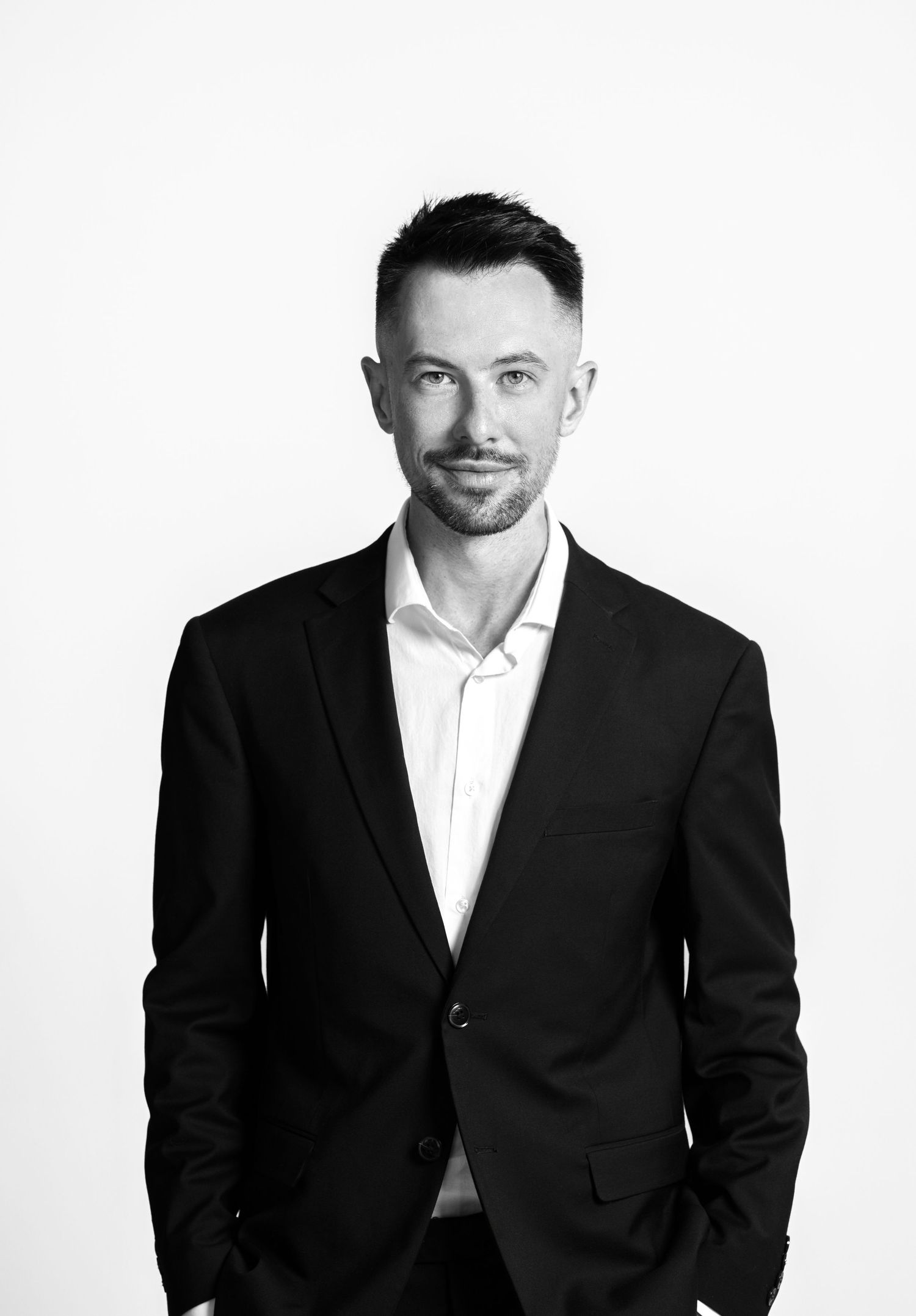 Black and white professional portrait of a person in a dark suit jacket and white shirt against a light background.