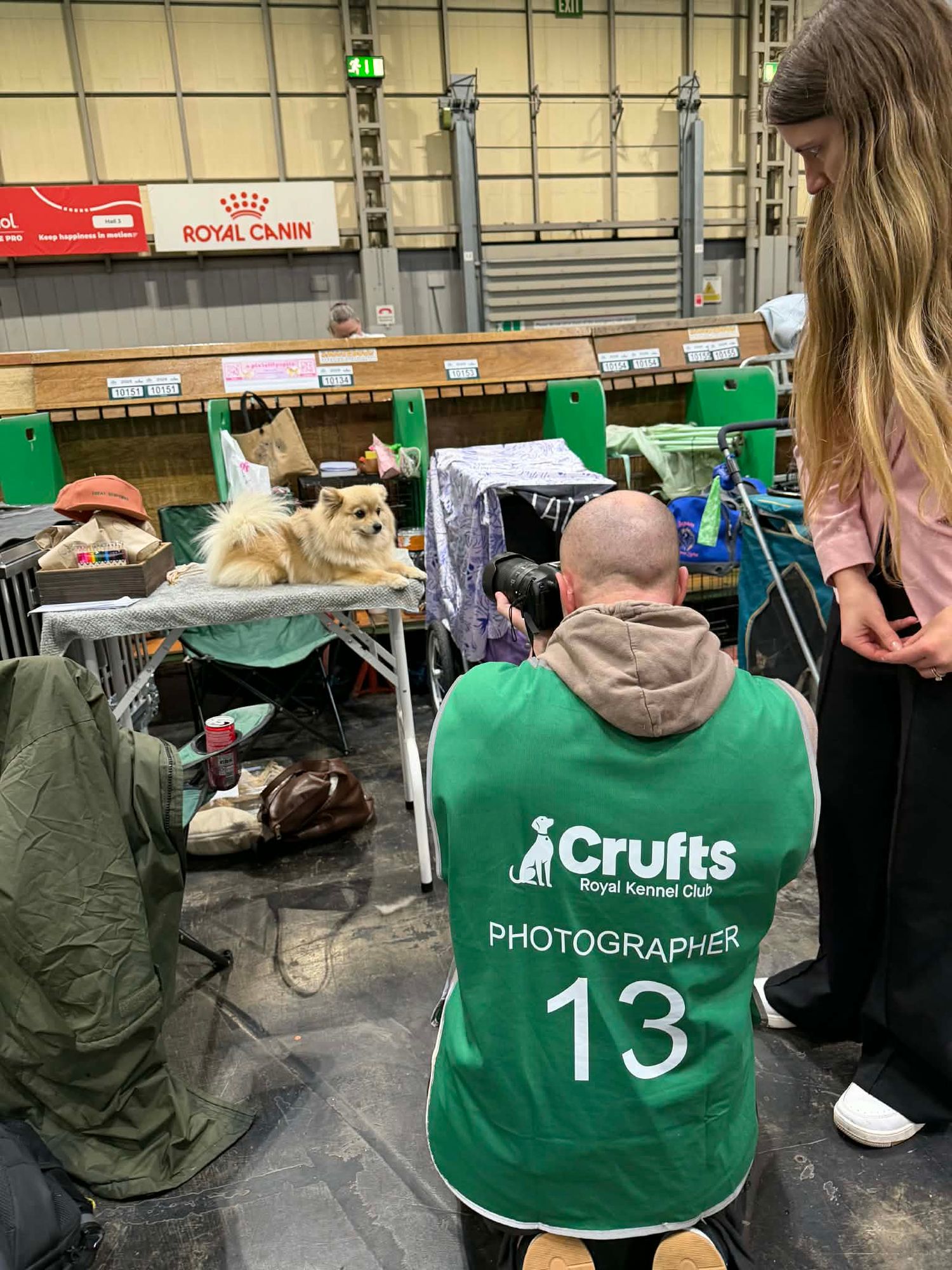 People in green Crufts photographer vests gather at a dog show venue with equipment and supplies.