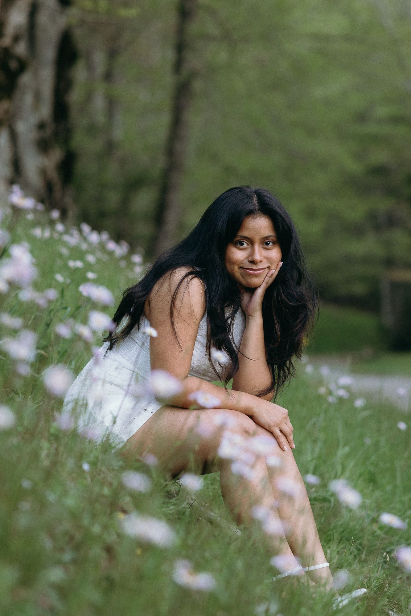 Woman in white dress sitting gracefully among wildflowers in a dreamy outdoor nature setting. The Bradford, Separk  Mansion, Graylyn Estate