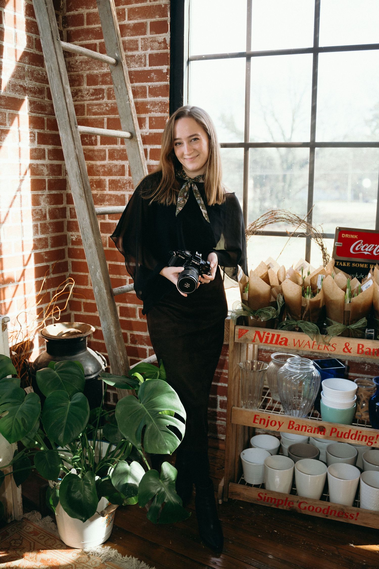 A photo series showing someone with a camera in a sunlit brick studio space with houseplants and vintage wooden crates.