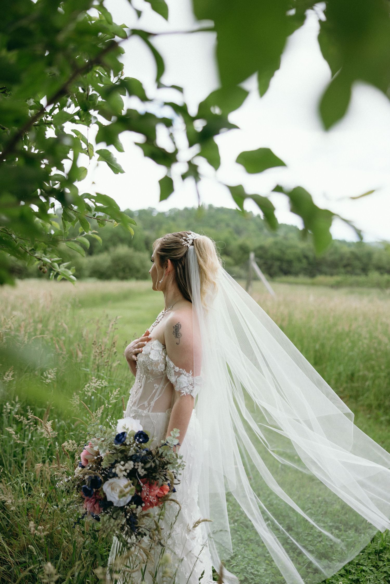 Bride in flowing veil holding colorful bouquet while standing in tall grass and greenery. The Graylyn Estate Wedding Photographer