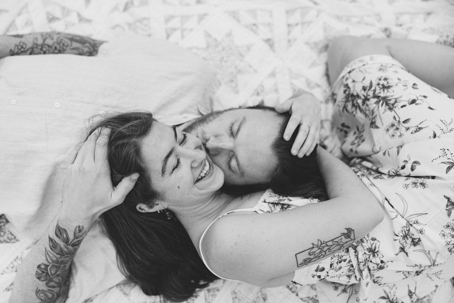 Black and white photo of two women laughing and cuddling together on a bed, sharing a joyful intimate moment.