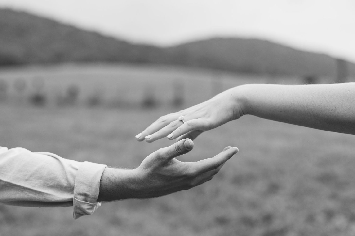 Two hands reaching toward each other against a mountain landscape in black and white. Luxury Estate Wedding Photographer in NC
