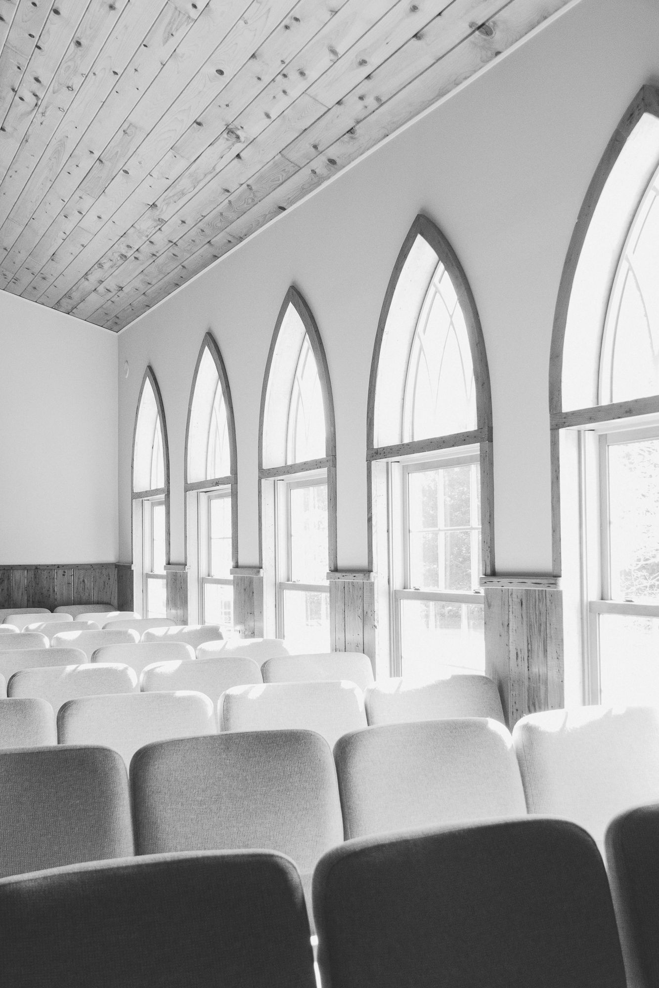 Interior of a chapel with arched windows and wooden pews in black and white. Luxury wedding photographer North Carolina