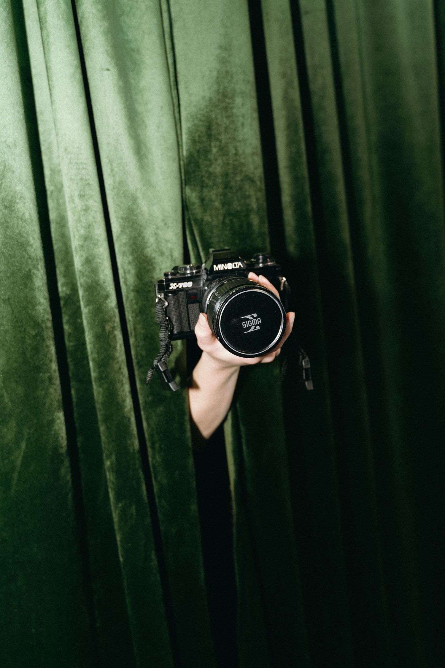 A hand holding a camera lens emerges from dark green forest background creating a mysterious artistic composition.
