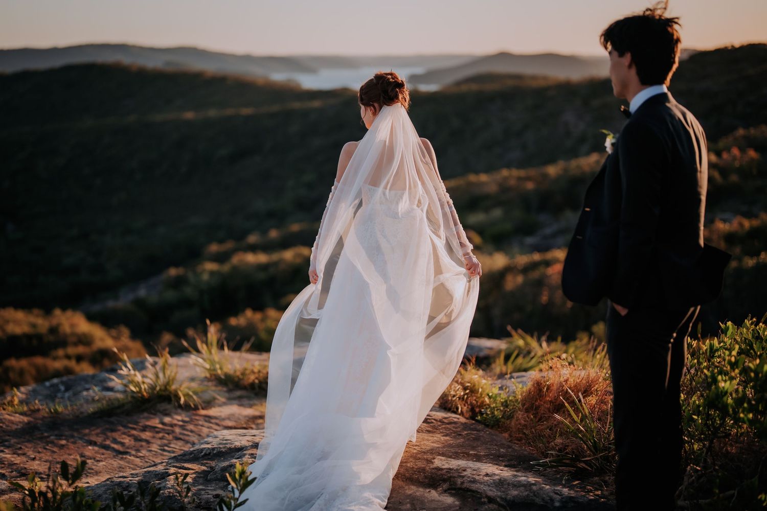 Dramatic sunset silhouette of flowing wedding dress veil against mountain backdrop.