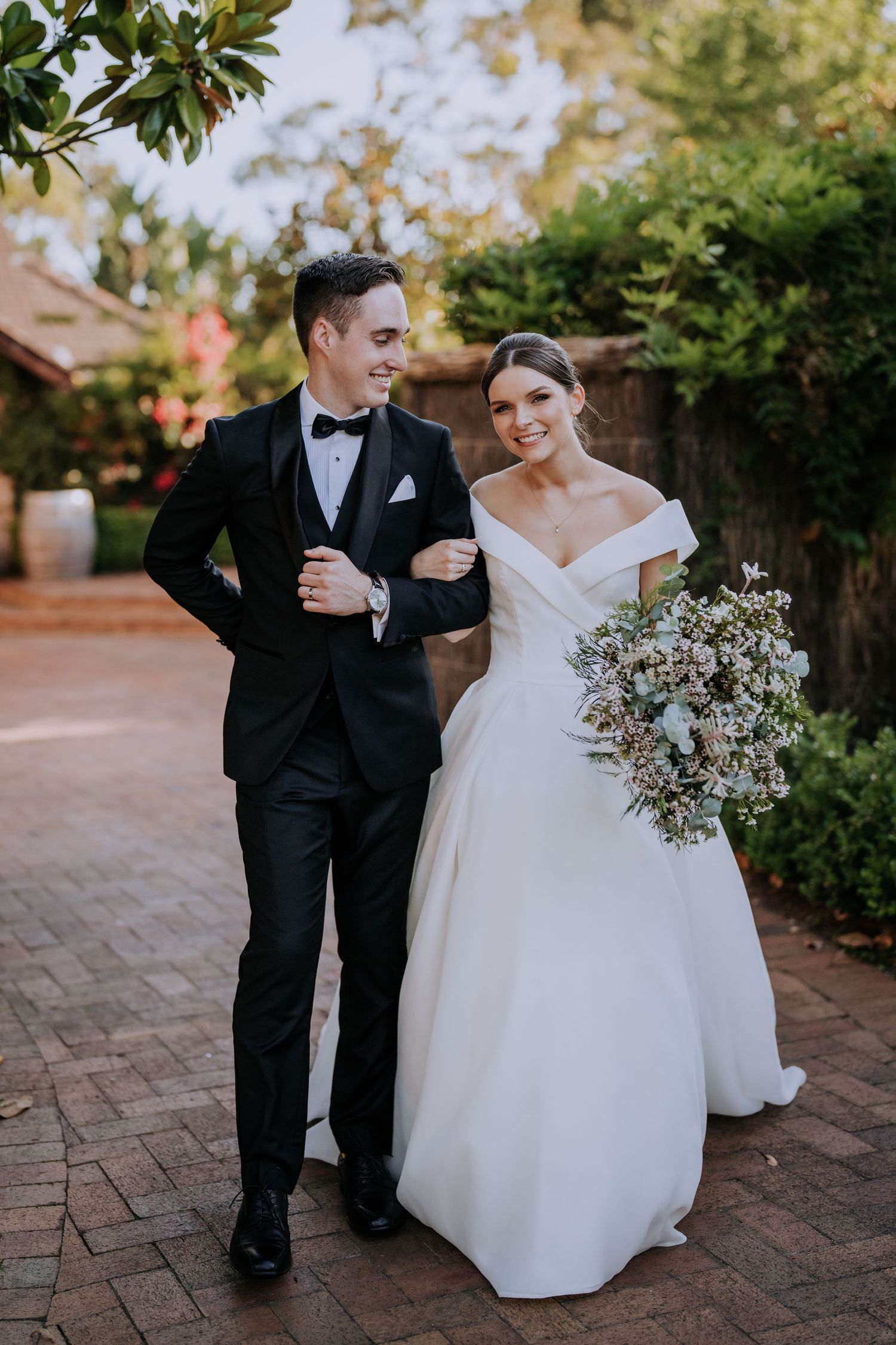 Couple walking along brick pathway surrounded by garden greenery.