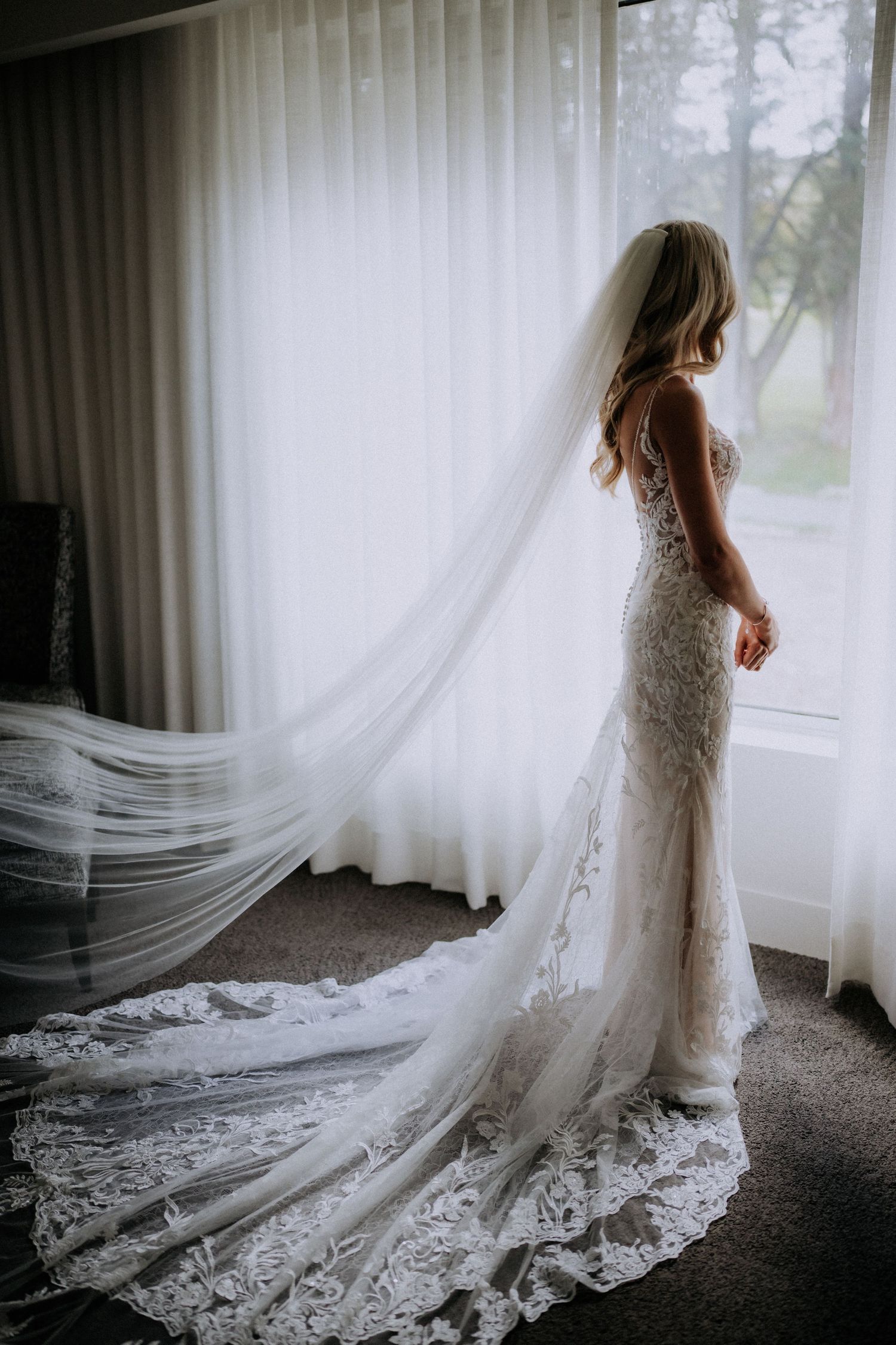 Silhouette of bride in lace gown with flowing train against window light.