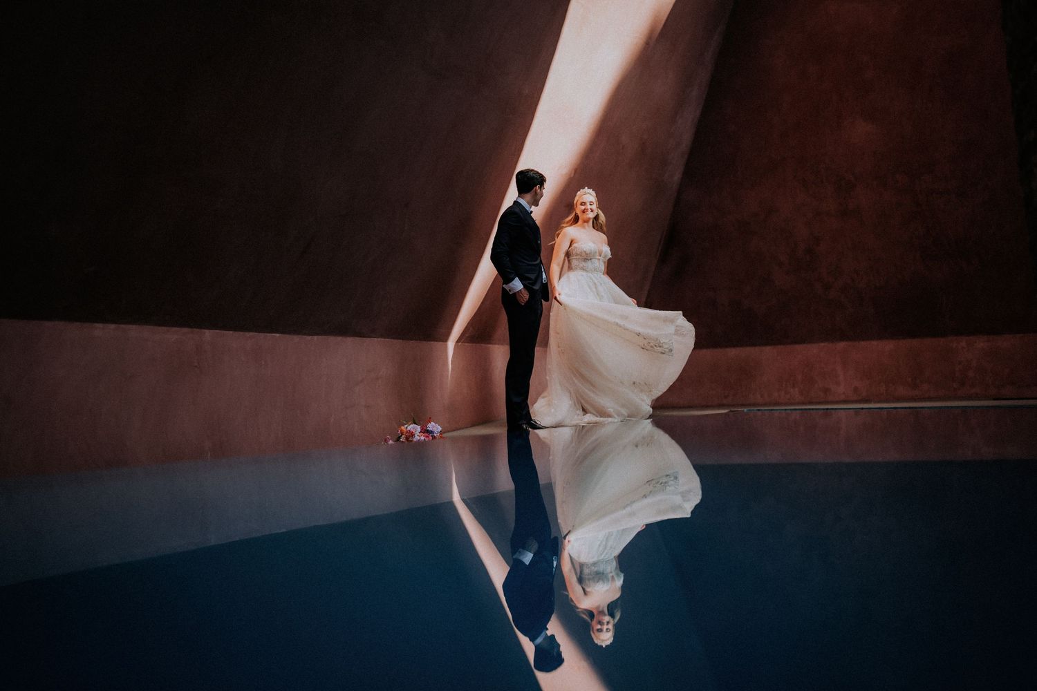 A couple dances together in a dramatically lit reception venue with reflective floor.
