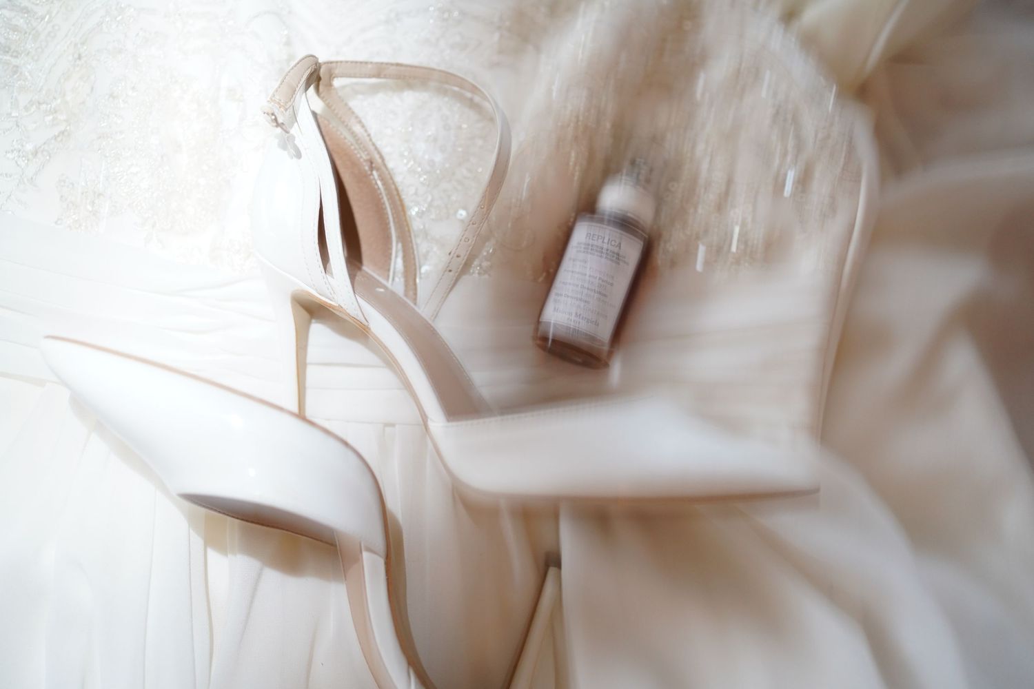Ethereal close-up of white bridal shoes and perfume bottle with dreamy lighting.