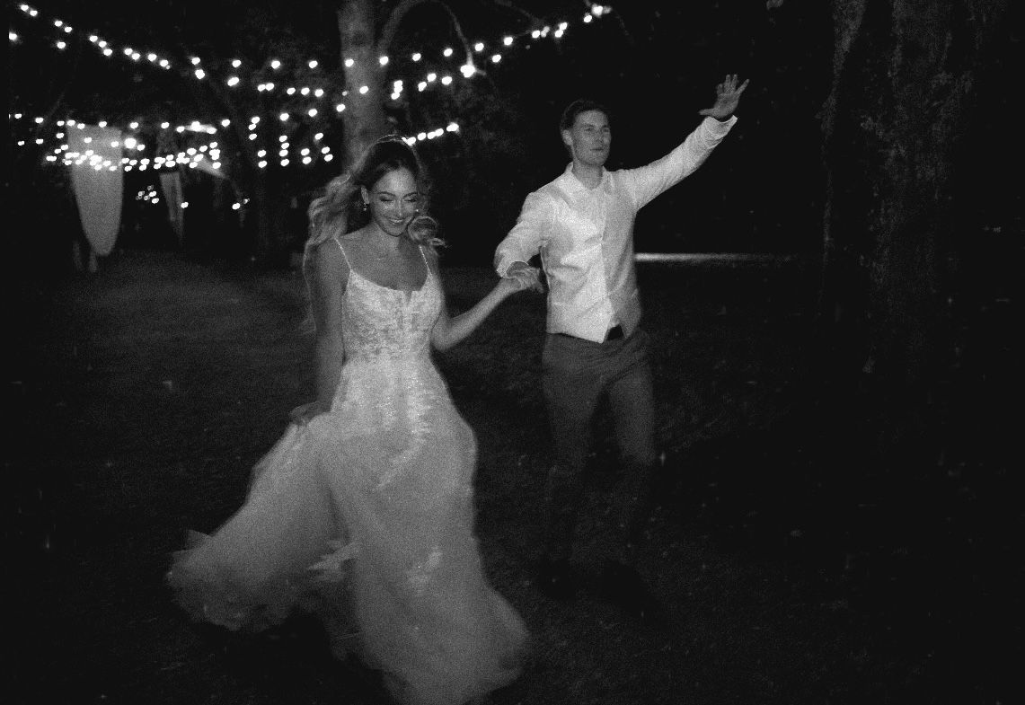 A couple dances joyfully under string lights at an outdoor evening wedding reception.