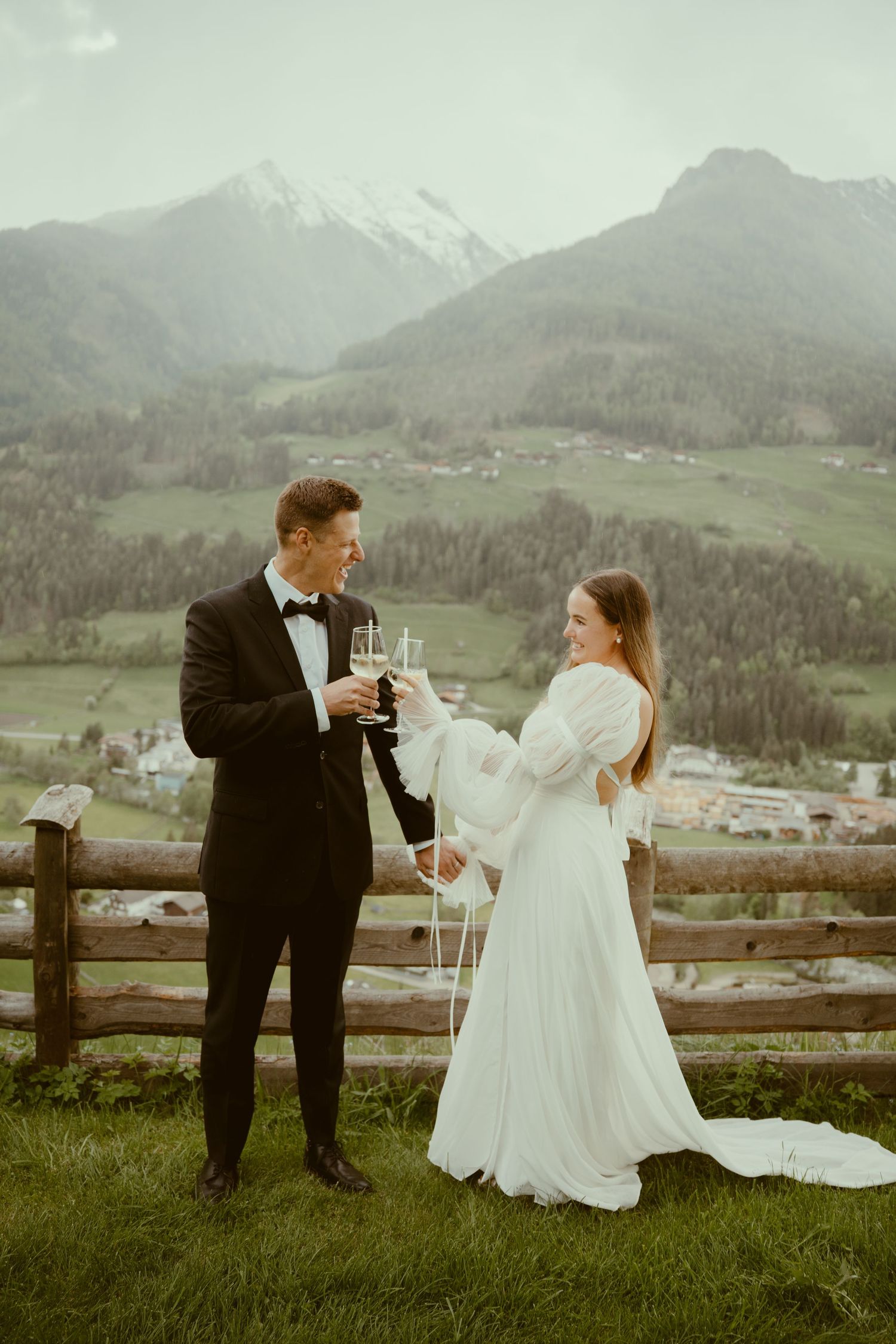 A couple shares an intimate moment on a grassy hilltop overlooking majestic snow-capped mountains in the distance.