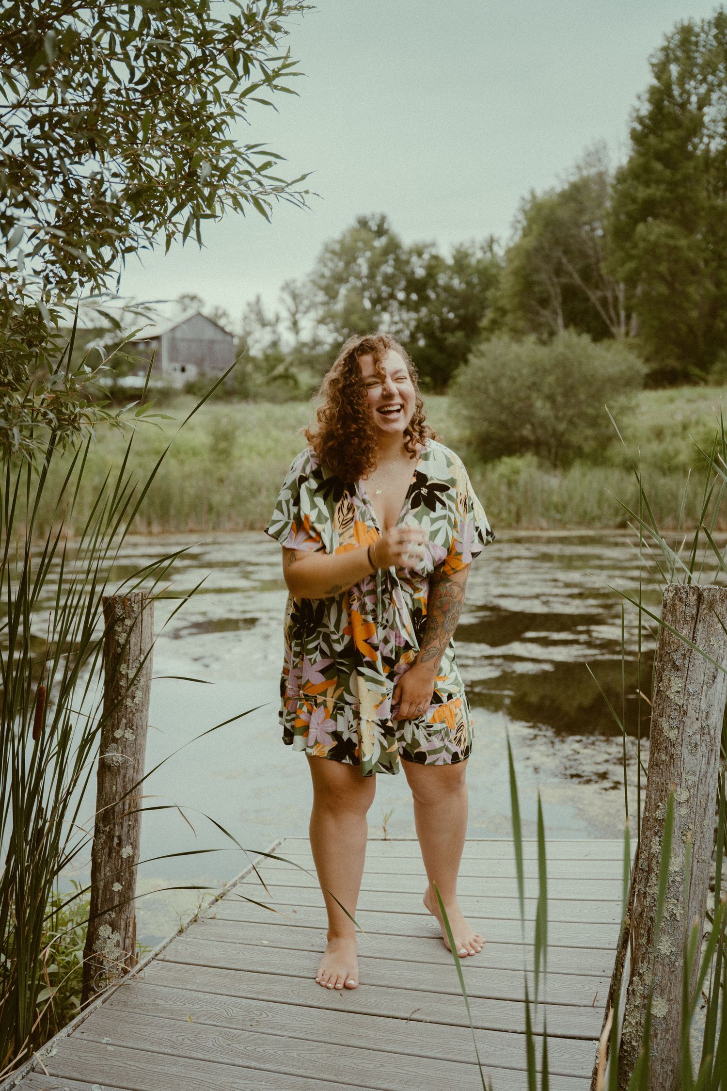 Summer portrait session at scenic lake dock with reeds and lily pads surrounding the wooden boardwalk in warm light.