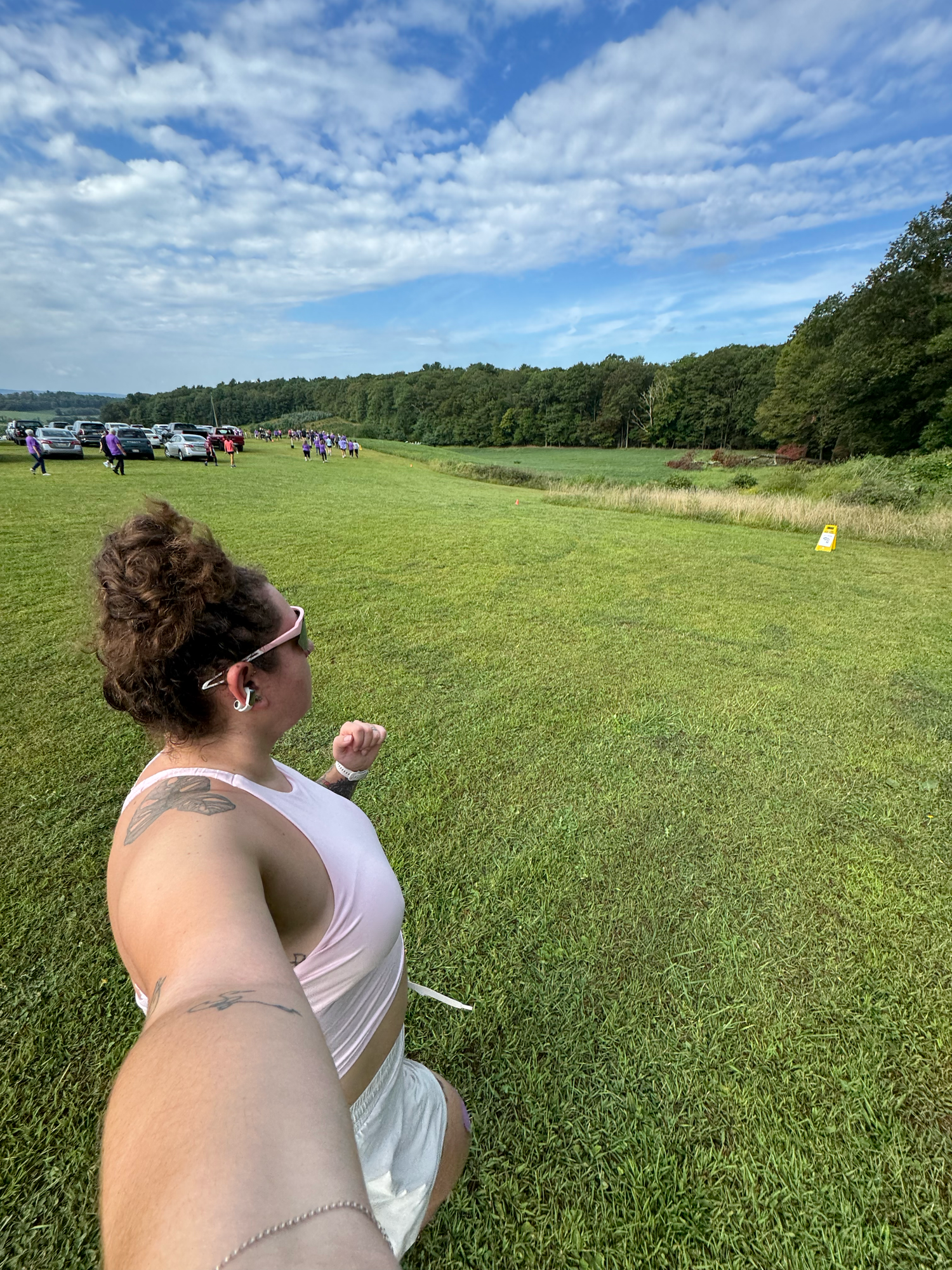 Someone in a white shirt throws a colorful disc through the air on a sunny day in a grassy field with blue skies above.