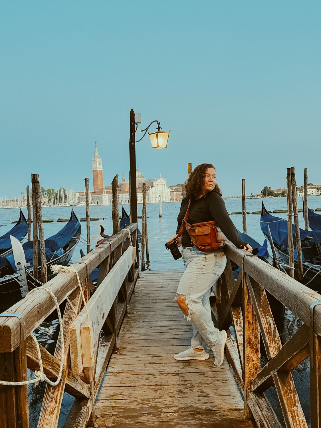 Tourist enjoying the scenic view of Venice from a wooden dock with traditional gondolas and San Giorgio Maggiore in view.
