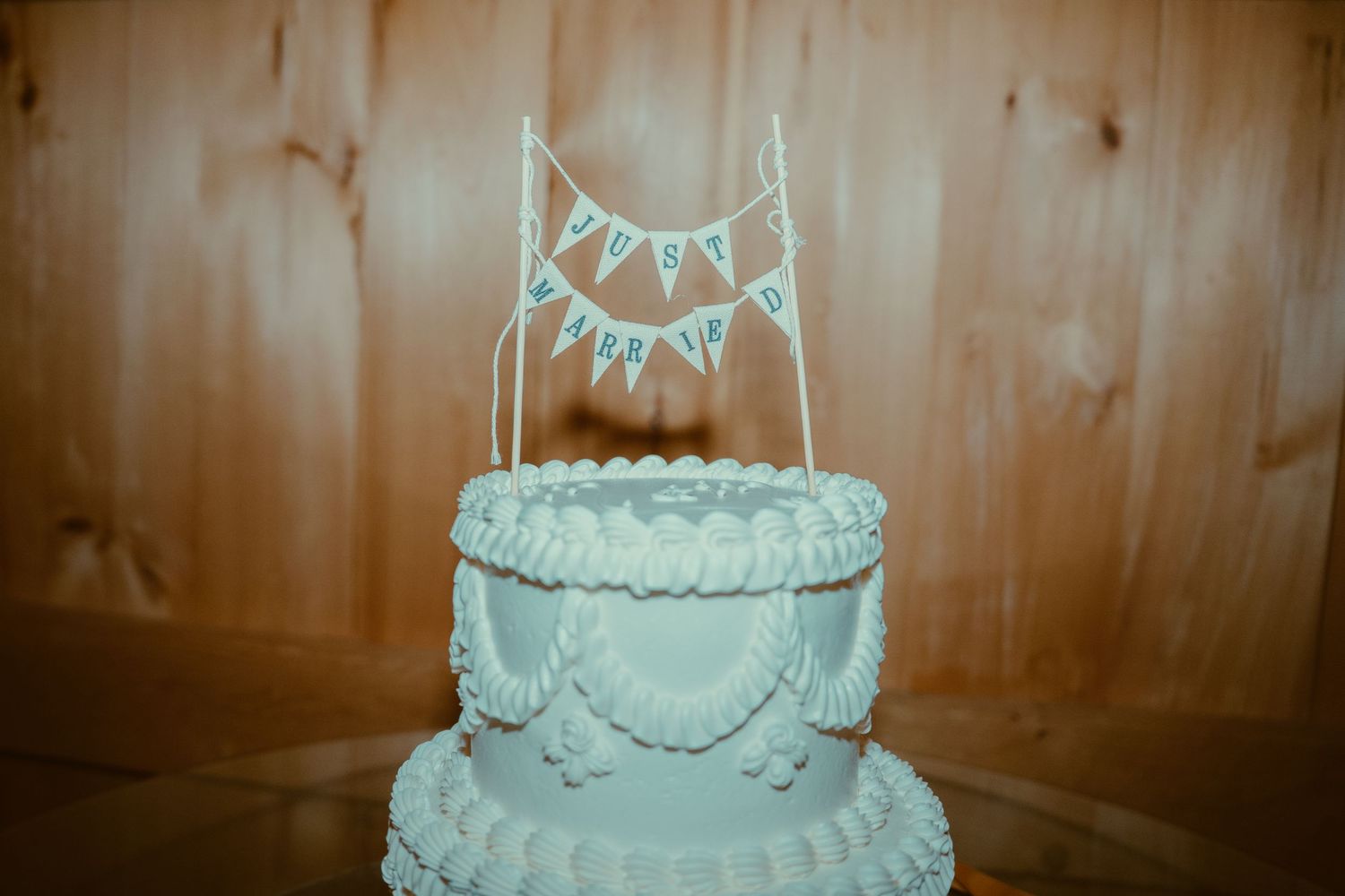A white wedding cake with multiple tiers decorated with delicate piping and floral accents sits on display.
