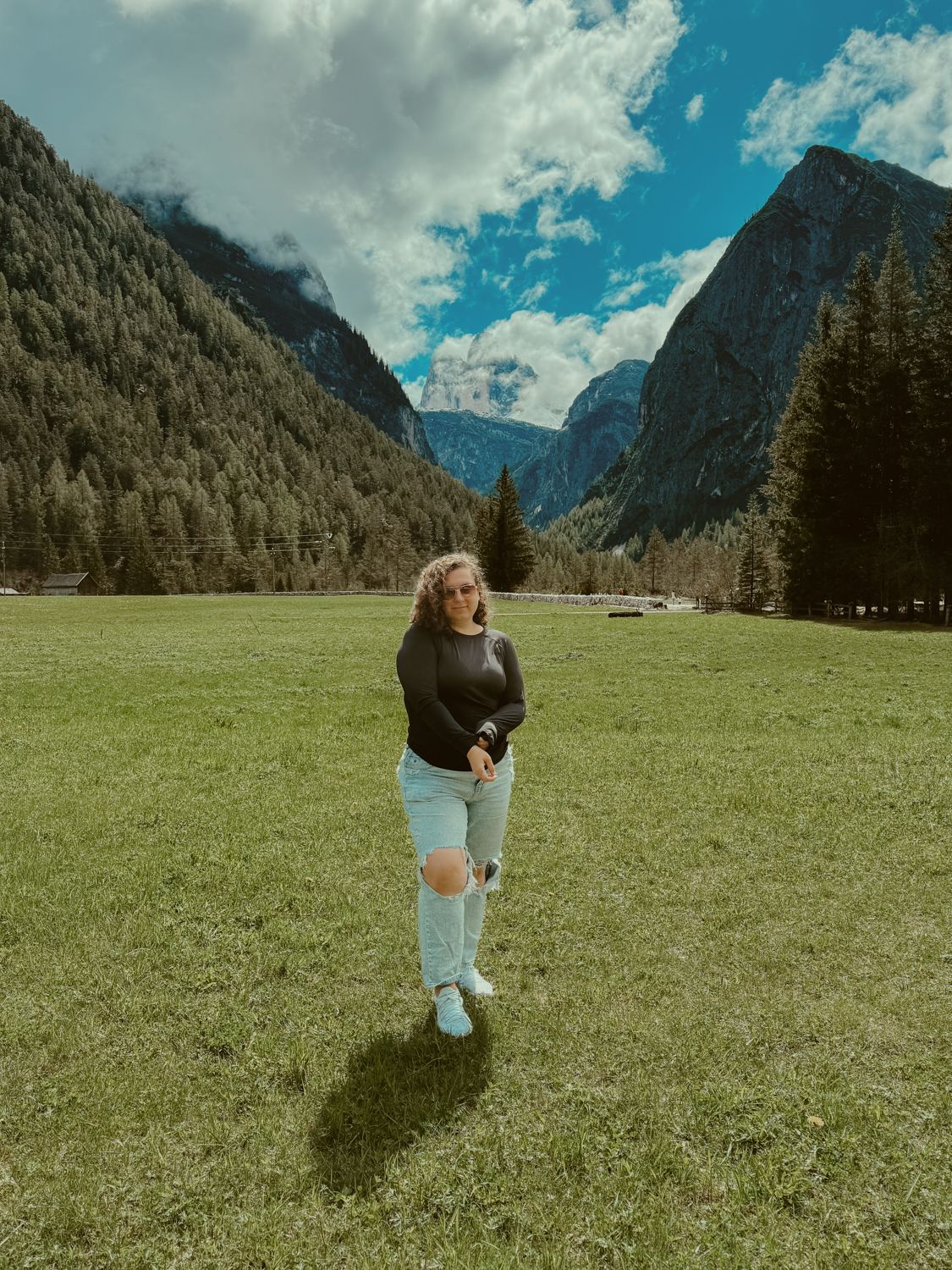 Someone stands in a grassy meadow with dramatic mountain peaks and evergreen forests in the backdrop at Yosemite National Park.