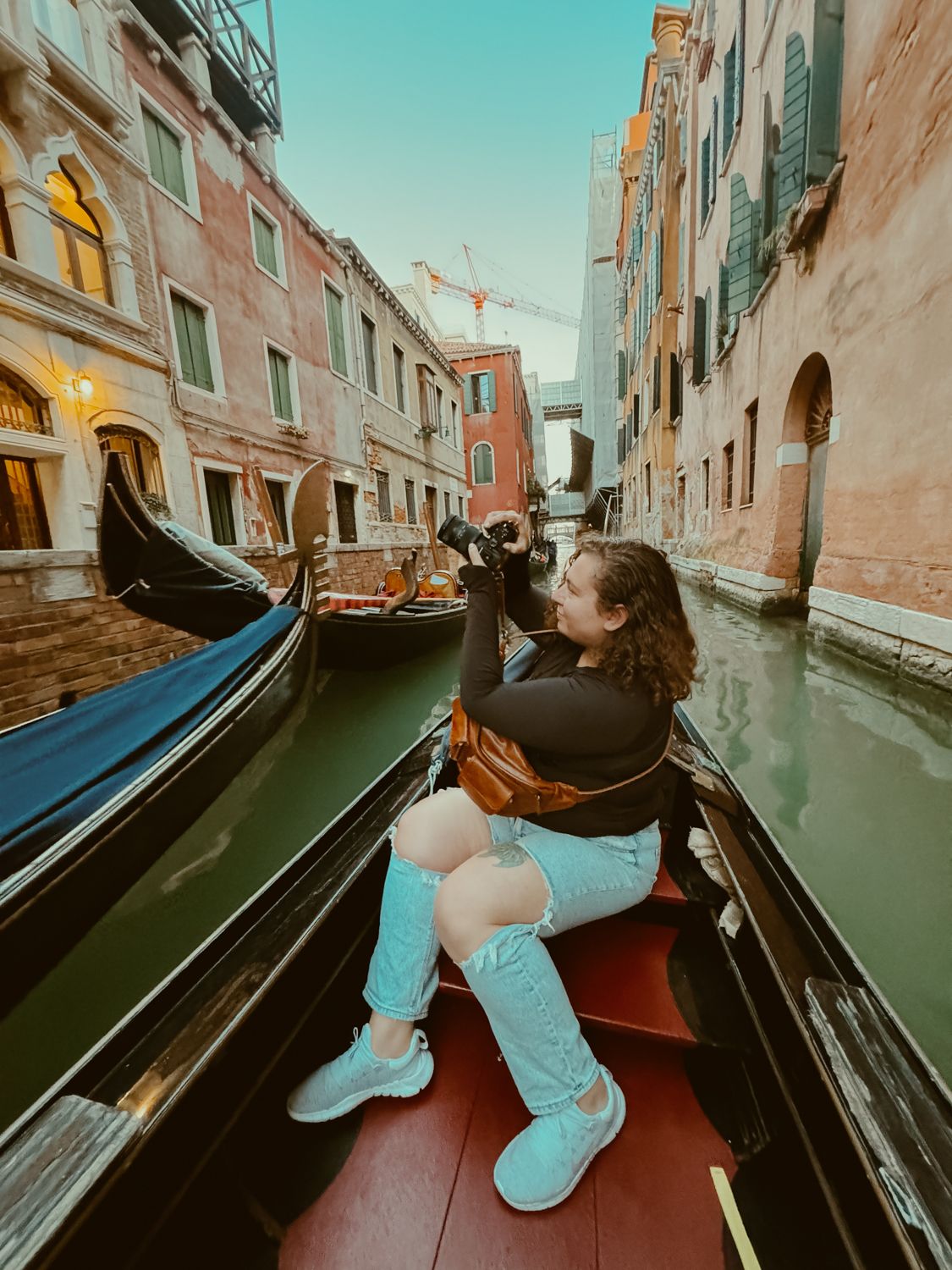 Tourist enjoying a scenic gondola ride through a narrow canal in Venice with historic buildings on either side.