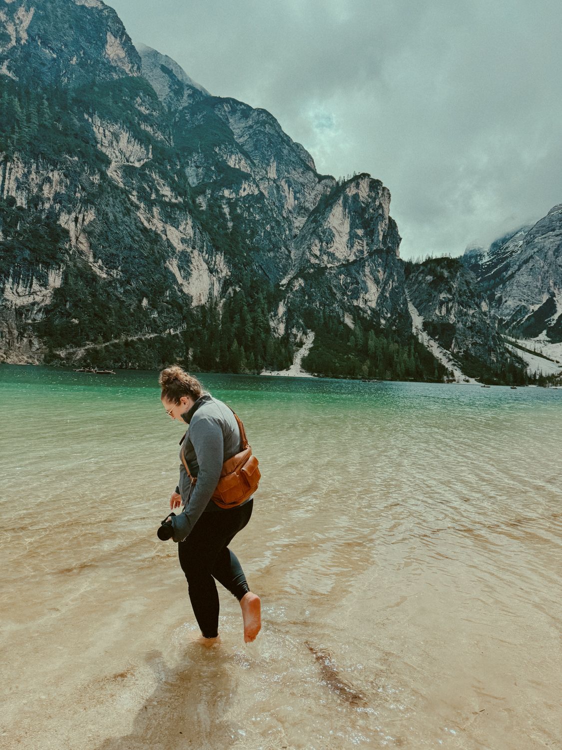 A traveler explores the turquoise waters of Lago di Braies in the Dolomites with dramatic mountain peaks in the background.