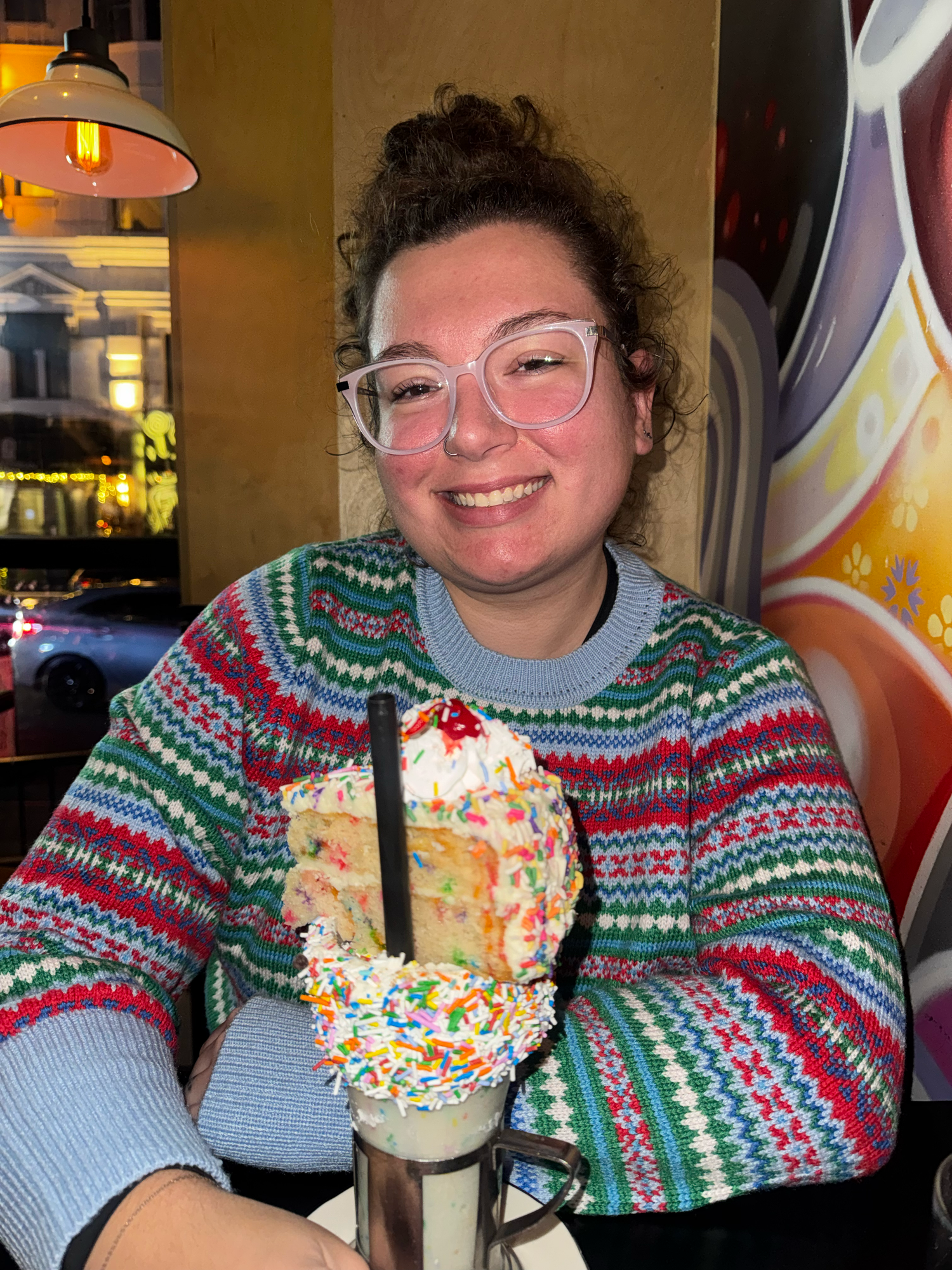 Someone wearing a festive Fair Isle pattern sweater in green and red sits at a table in a restaurant setting.