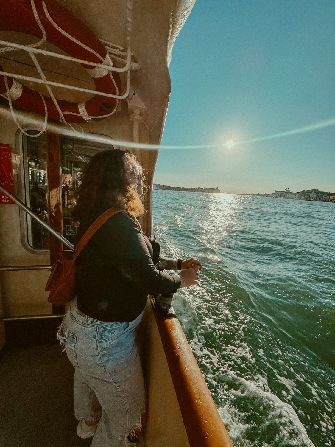 Passenger enjoying scenic boat ride on sparkling water during golden sunset hour by harbor shoreline.