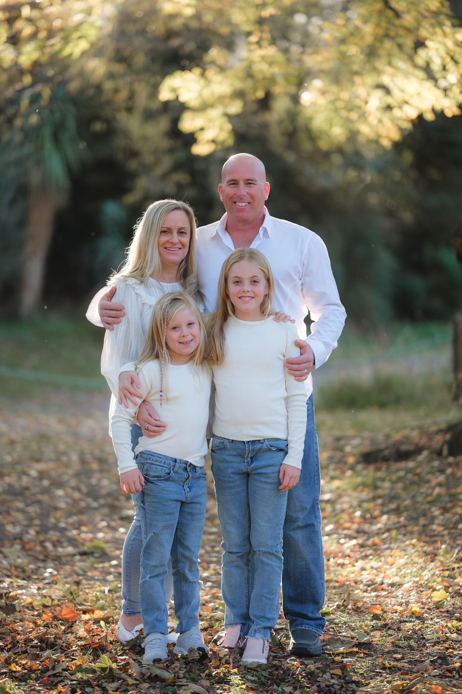 Family wearing coordinated white and denim outfits poses together on fallen autumn leaves.