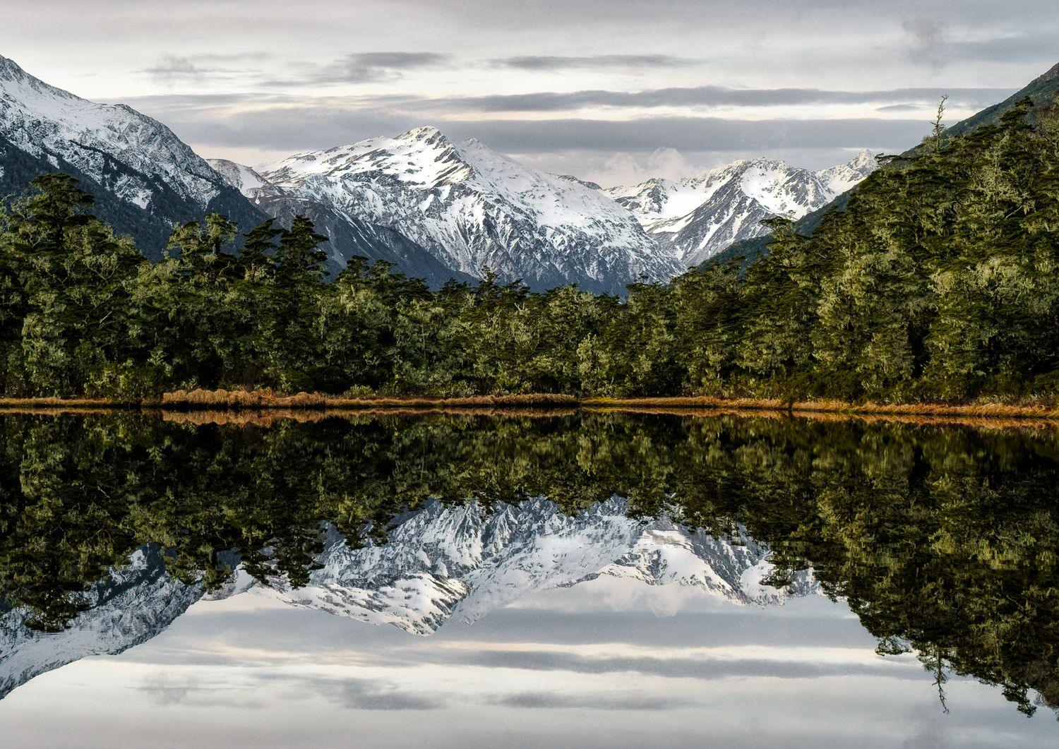 Panoramic view of snow-capped mountains reflecting in calm lake waters.