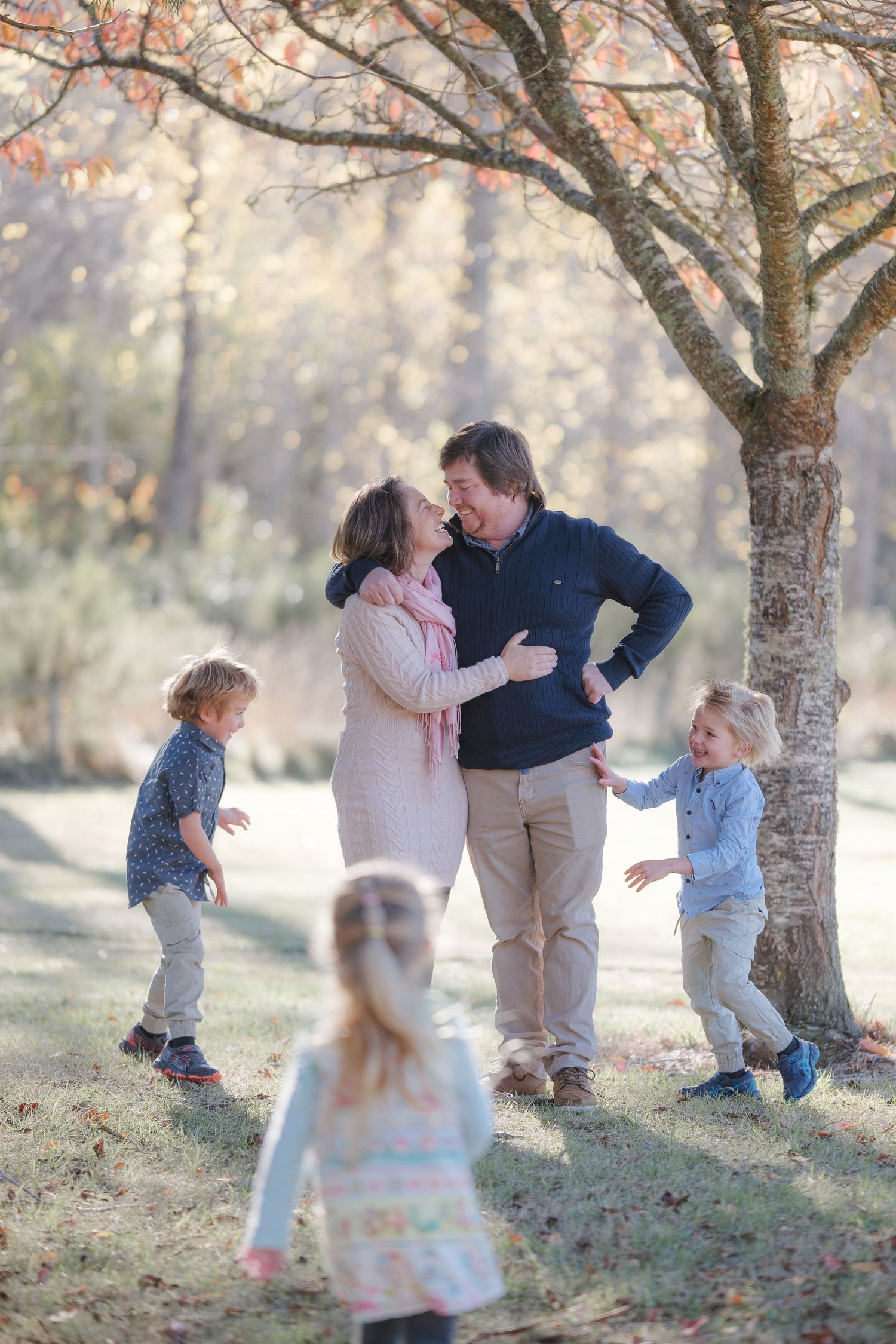 Family playing together under autumn trees in a candid series of outdoor photos.