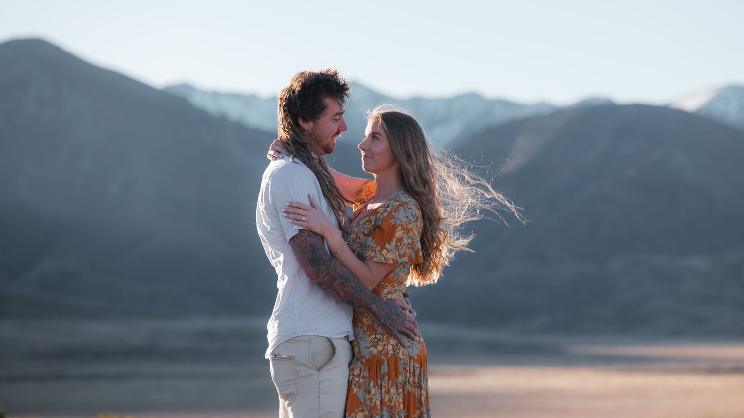 Couple embracing against mountain backdrop during sunset photoshoot.