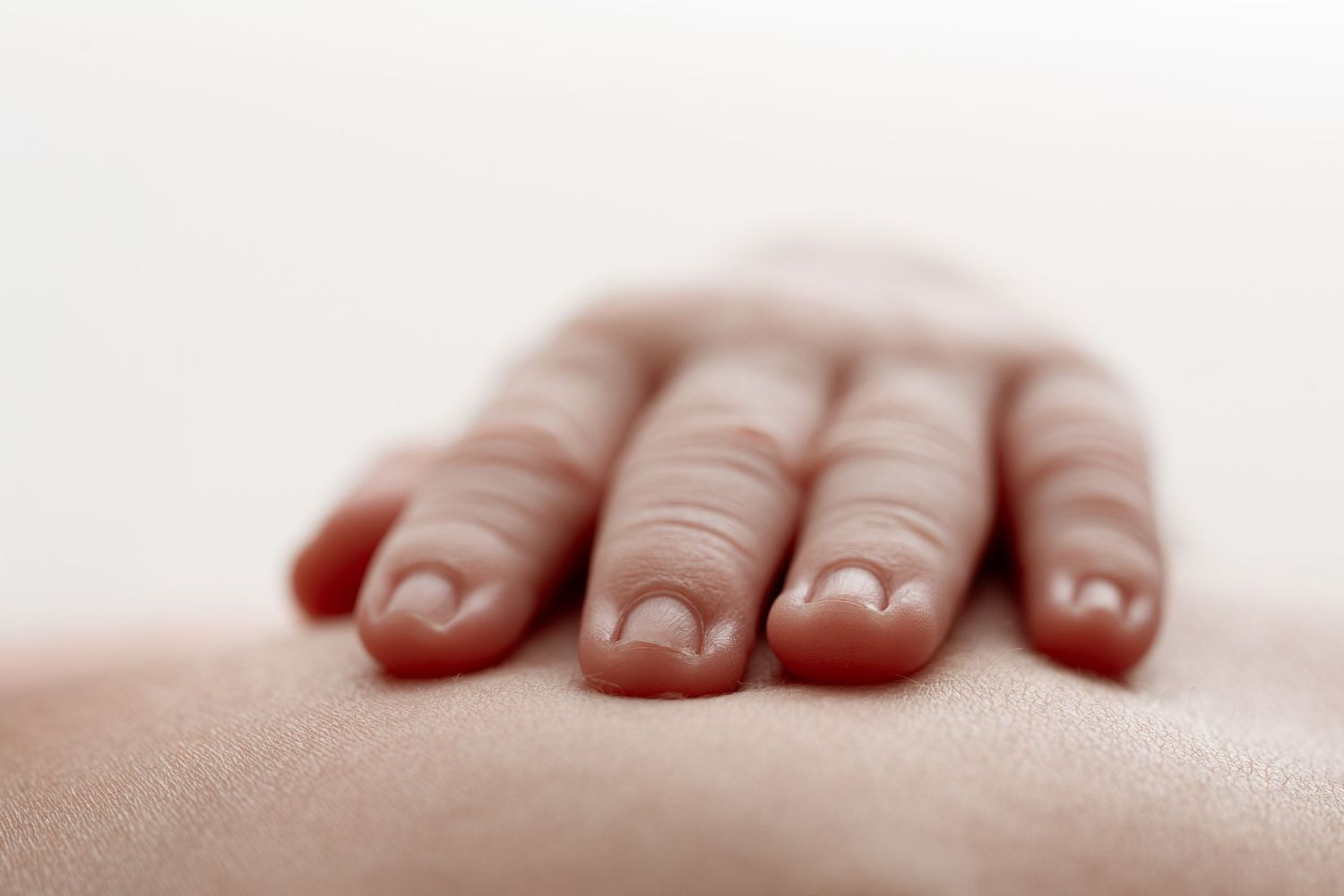 Close-up of a hand with fingers gently resting on smooth skin, showcasing natural nails and soft lighting.
