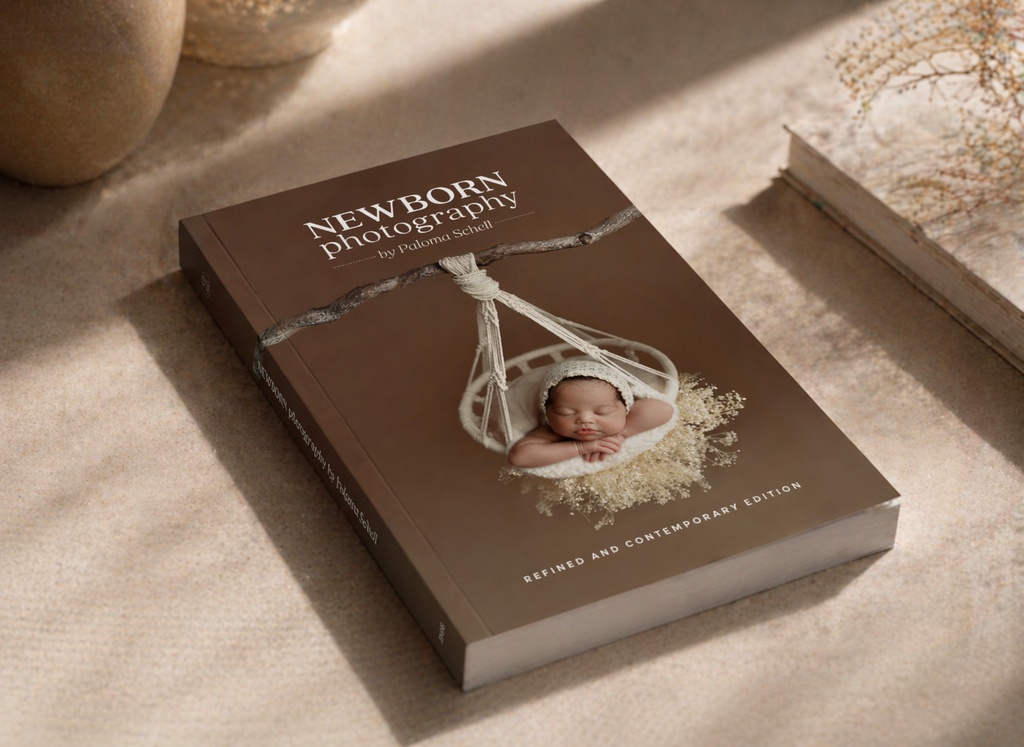 Brown hardcover newborn photography book with a sleeping baby on the cover, placed on a neutral linen surface.