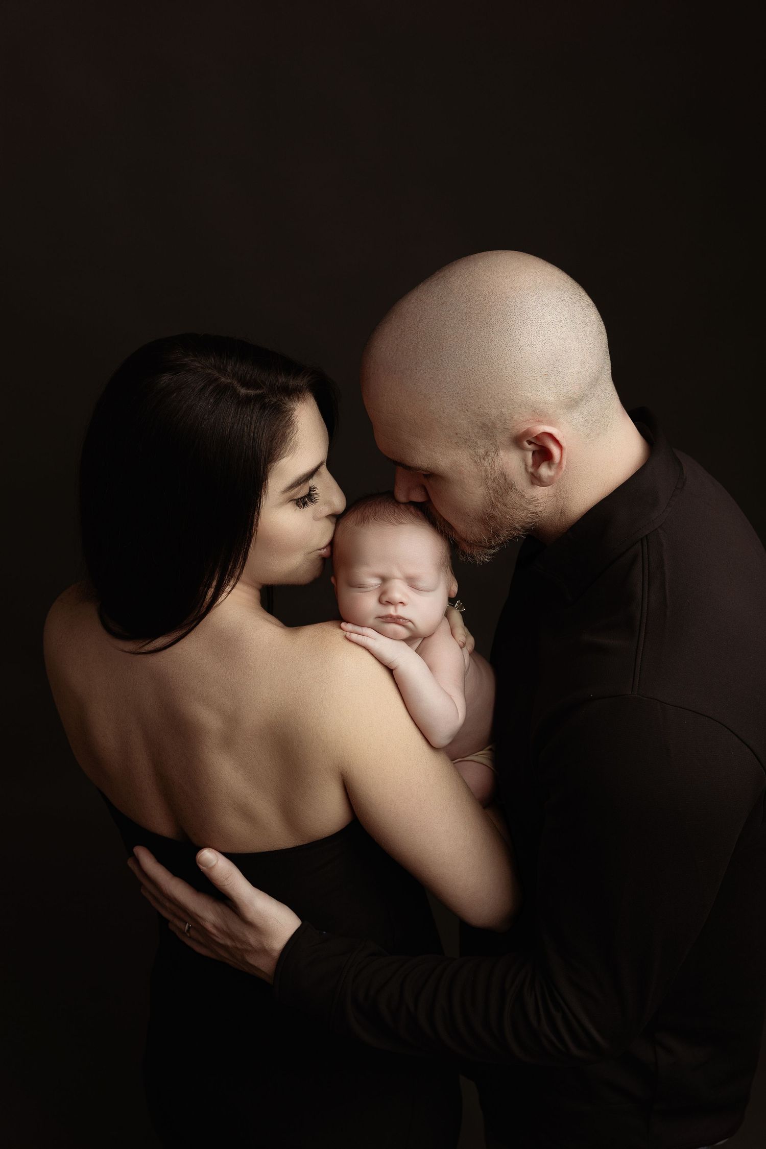 A artistic series of intimate black and white family portraits with a newborn baby set against dark background.