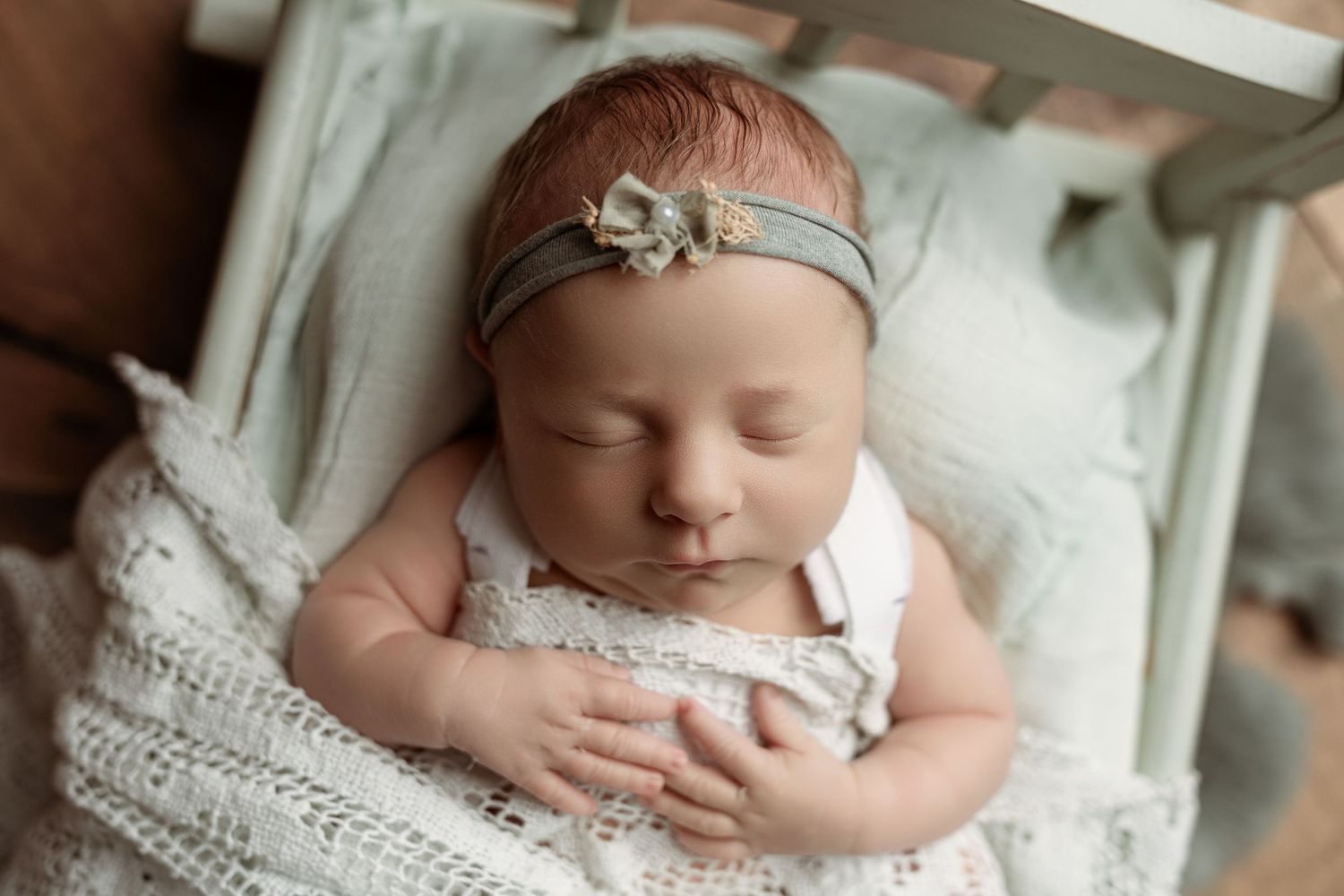 Sleeping newborn baby in white lace wrap and delicate headband lies peacefully on soft blanket– newborn photographer Paloma Schell Houston