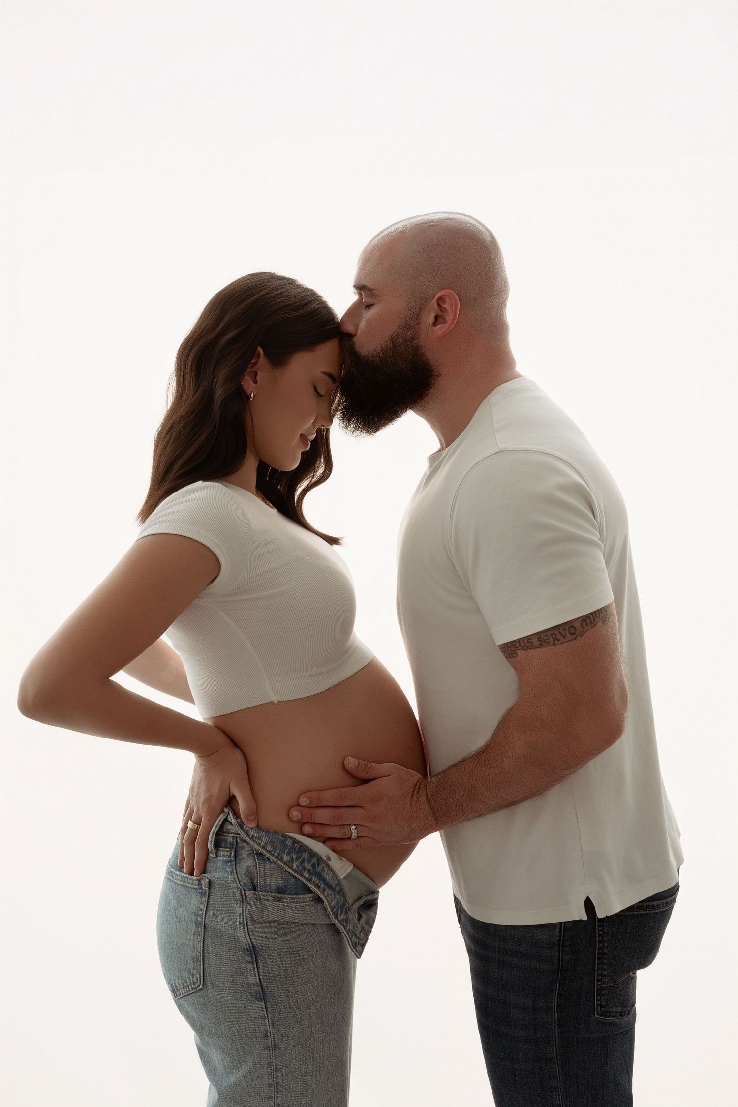 A couple shares an intimate moment during a maternity photoshoot against a white backdrop. maternity photographer Paloma Schell Houston TX
