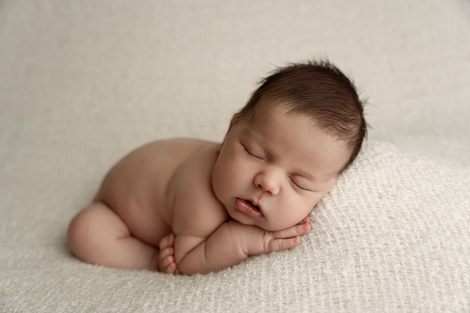 A peaceful newborn baby sleeping on a soft white blanket in a classic posed newborn photography portrait.