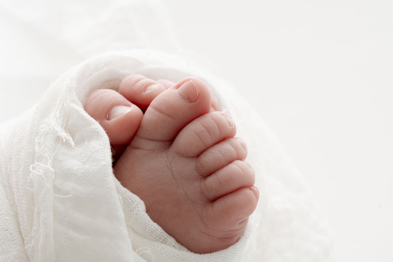Close-up of tiny newborn baby feet wrapped in soft white blanket, perfect infant toes detail photo.
