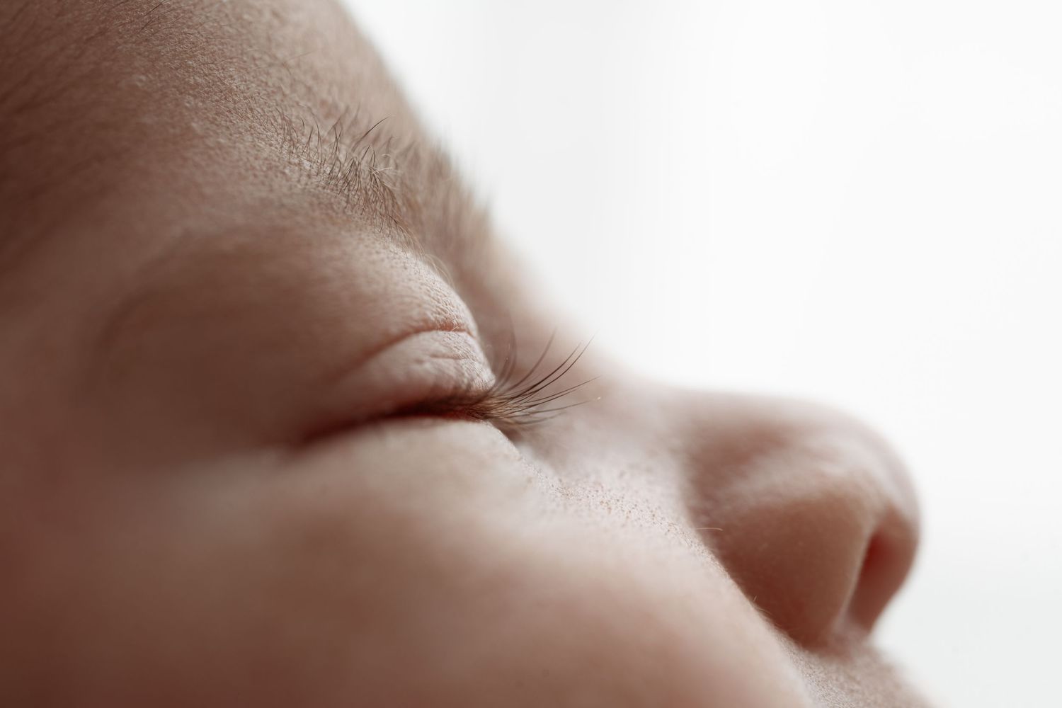 Close-up of a sleeping newborn baby's face showing delicate eyelashes, soft skin, and tiny nose.