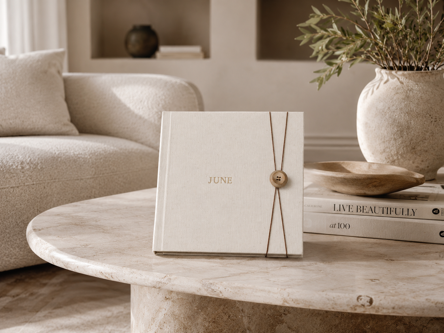 Elegant cream linen journal with gold wax seal on marble coffee table in minimalist neutral living room.