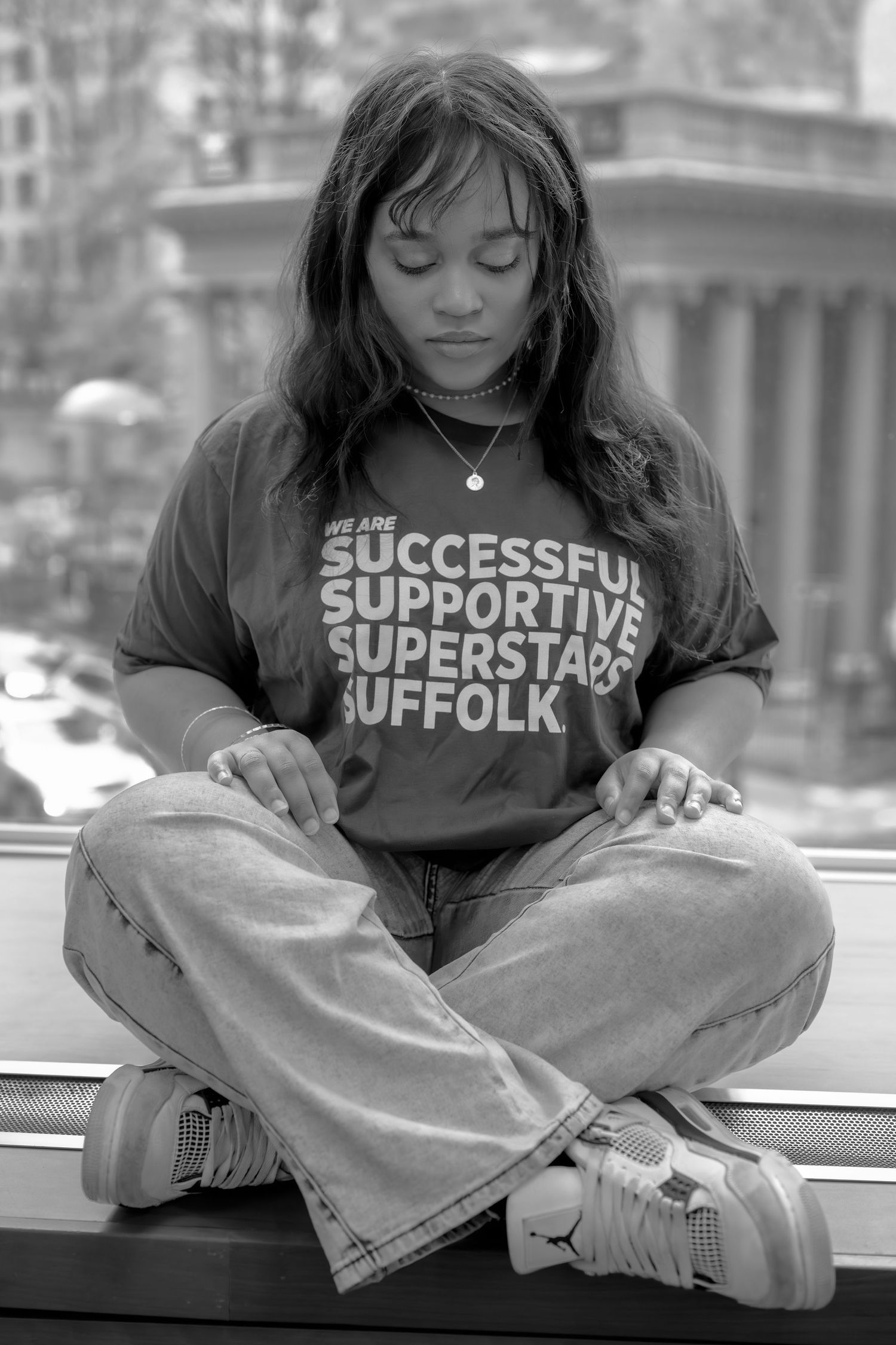 Young woman meditating cross-legged on a windowsill wearing a Suffolk University t-shirt, black and white photo.