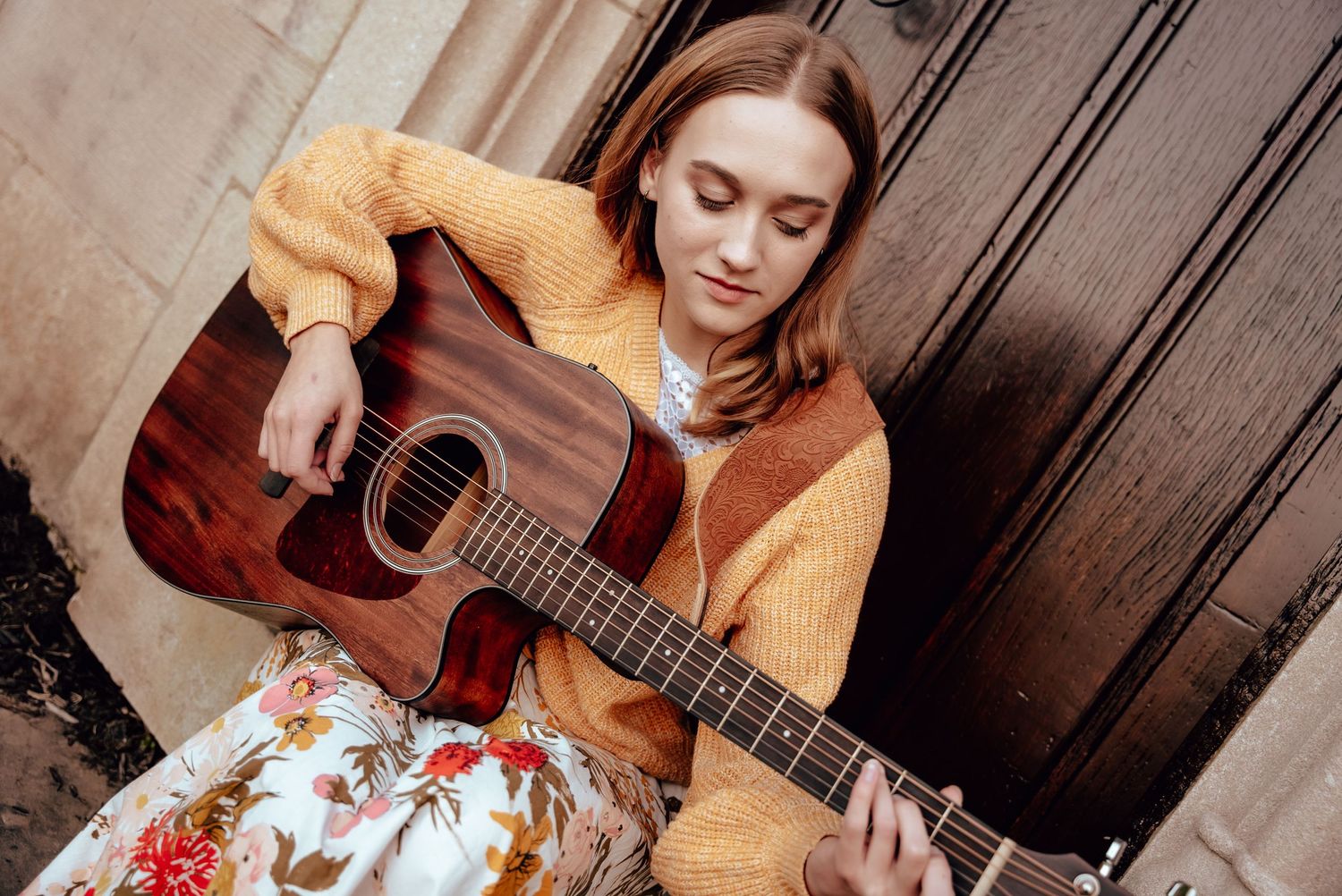 Musician playing acoustic guitar during an outdoor senior portrait session.