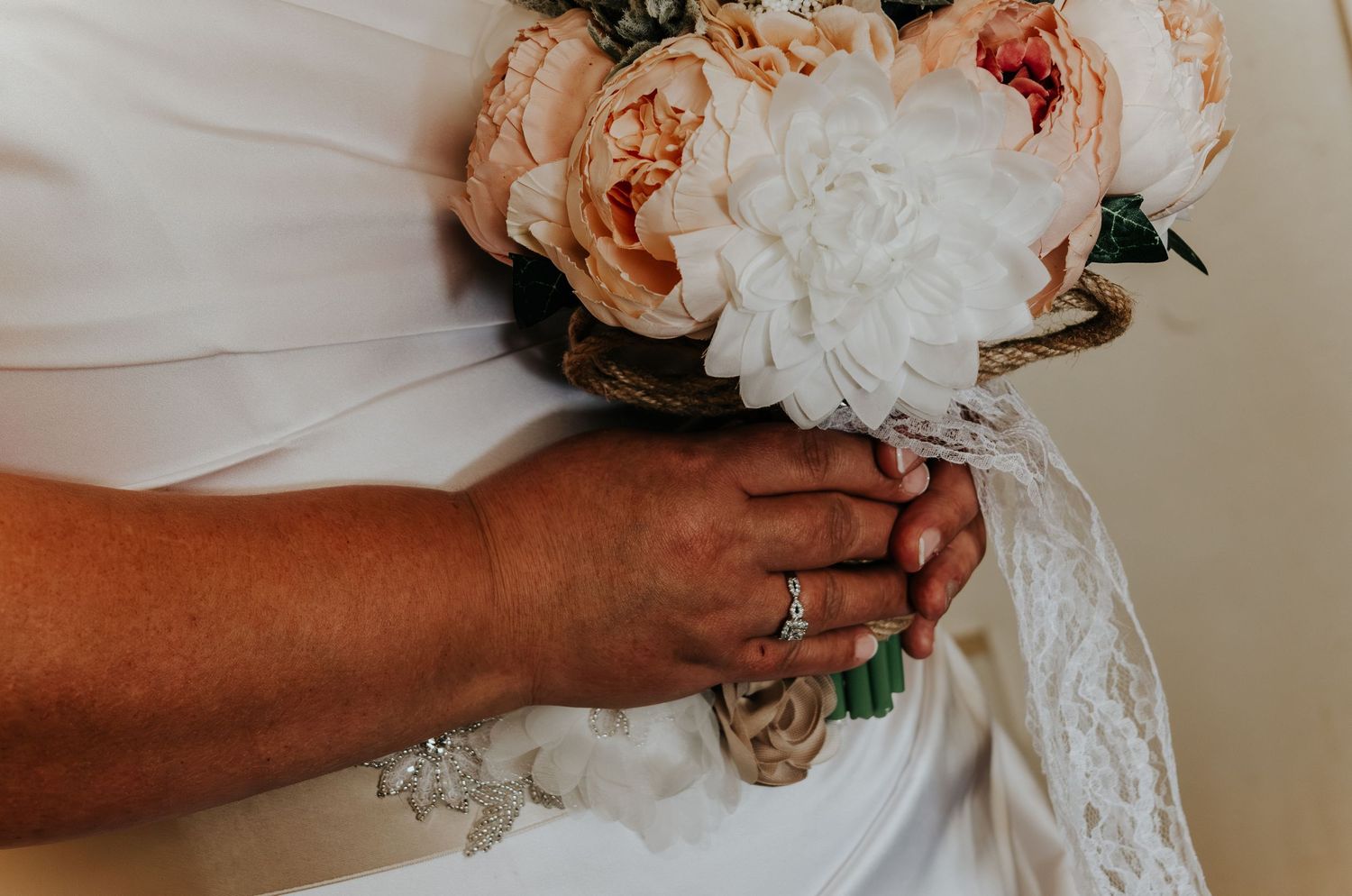 A delicate white and peach wedding bouquet with roses and lace trim being held against a light background.